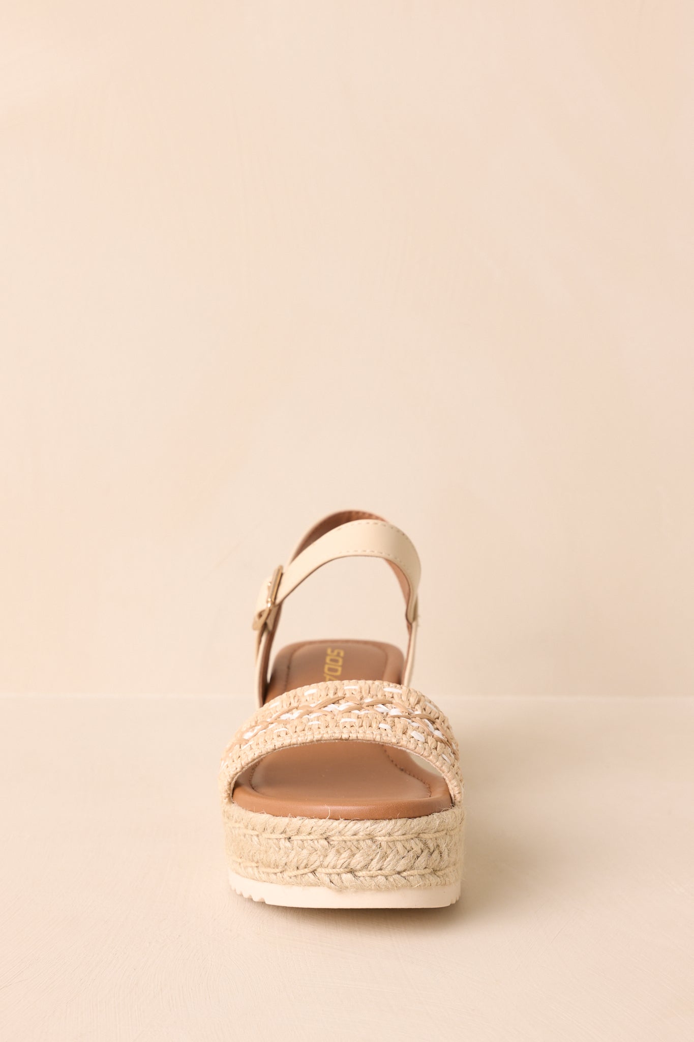 Front view of the raffia sandals displayed on a beige background showing the woven vamp strap and wedge silhouette.