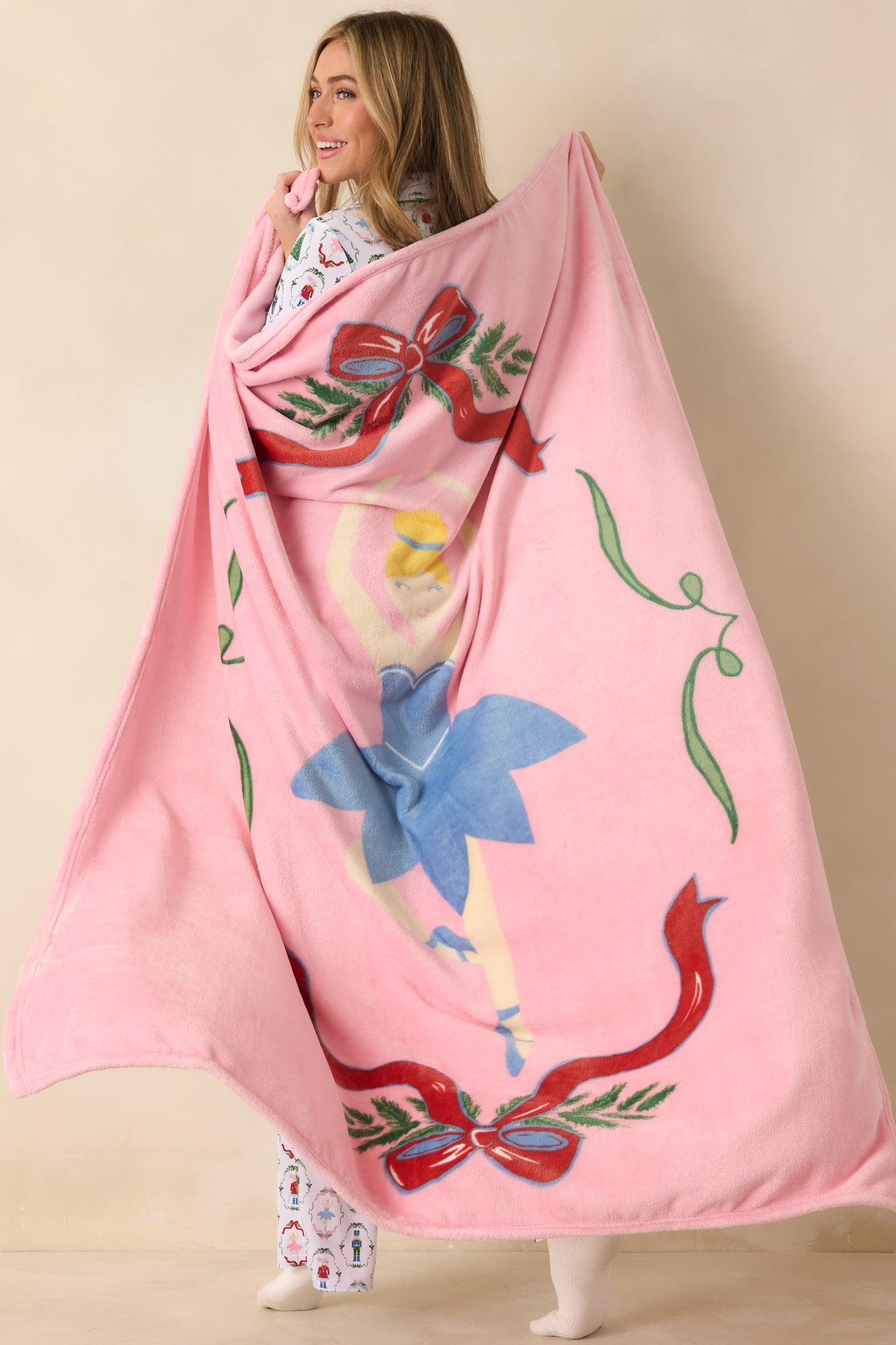 Front view of the light pink throw blanket showing the ballerina motif framed with festive ribbon and greenery accents.