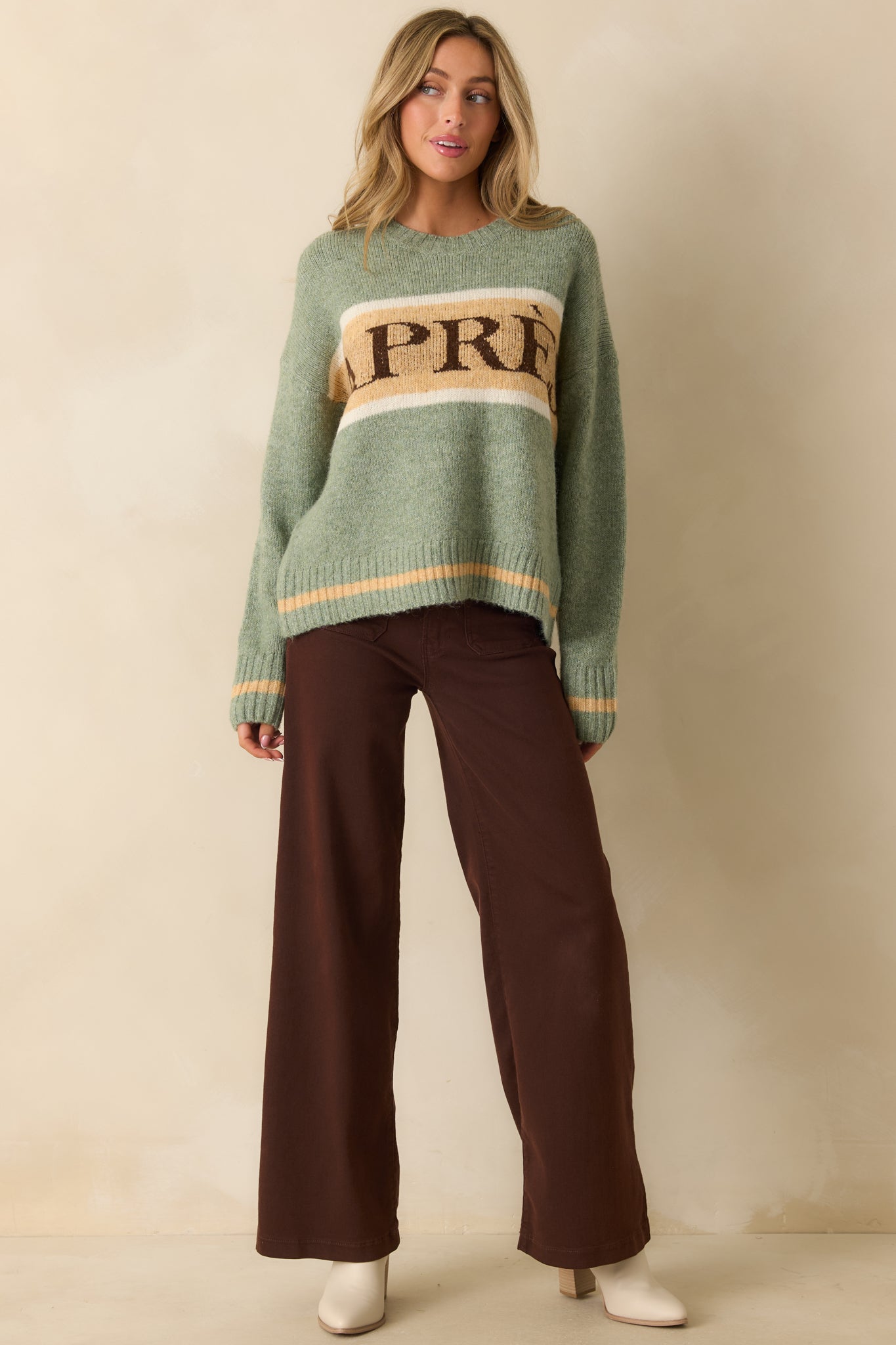 Front-facing view of the sage green knit pullover sweater highlighting the relaxed fit, ribbed trim, and “APRÈS” striped chest detail.