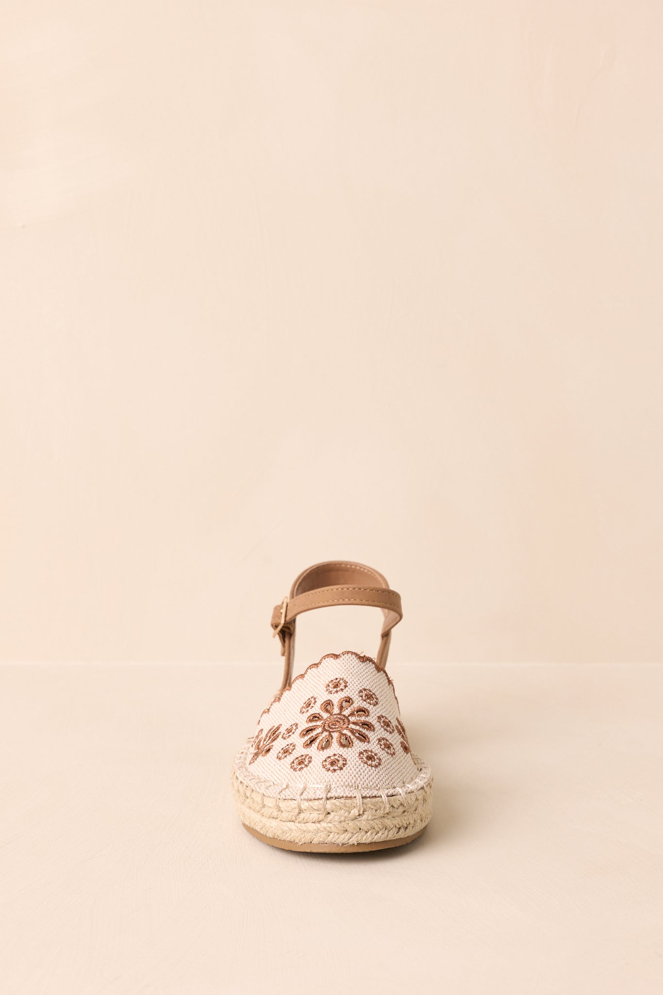 Close front view of the flat sandals showing the rounded canvas closed-toe design with brown embroidered eyelet detailing.