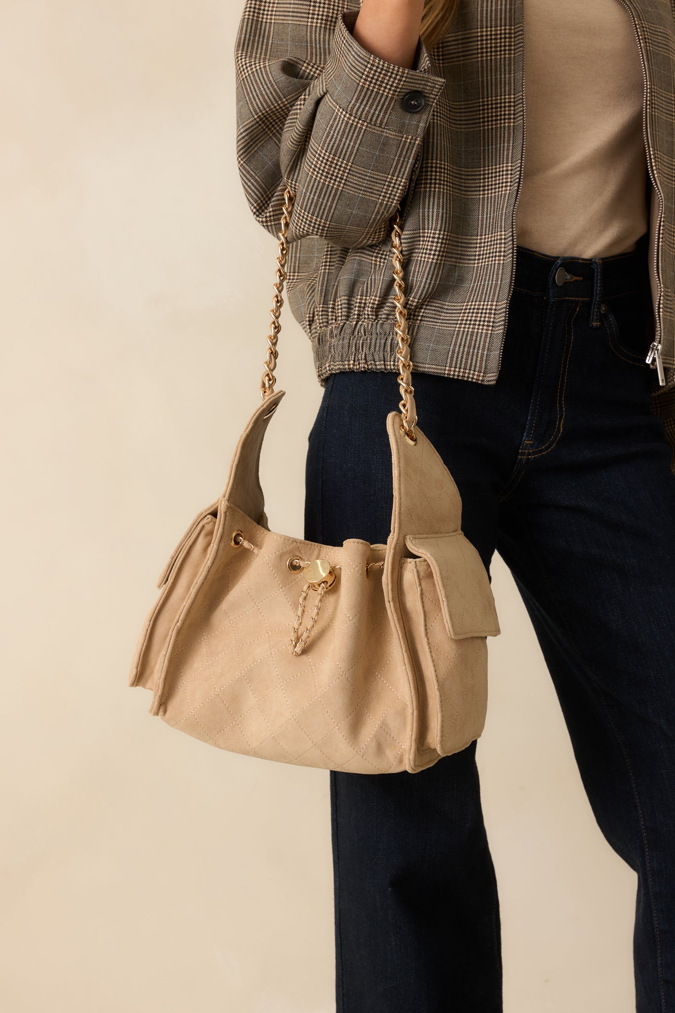 Front view of taupe purse highlighting the quilted texture, gold grommet details, and woven drawstring closure.