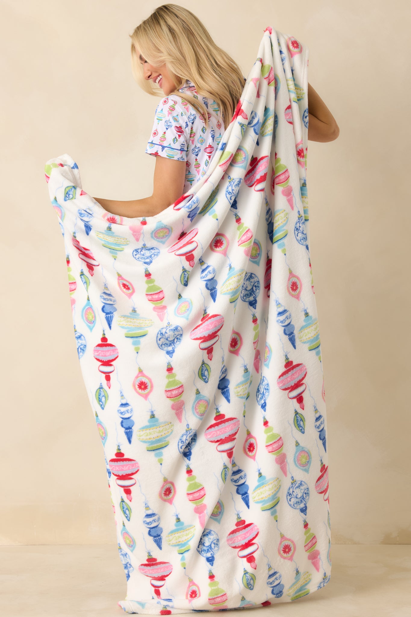Front view of the white throw blanket showing the colorful allover ornament print in red, blue, green, and pink.