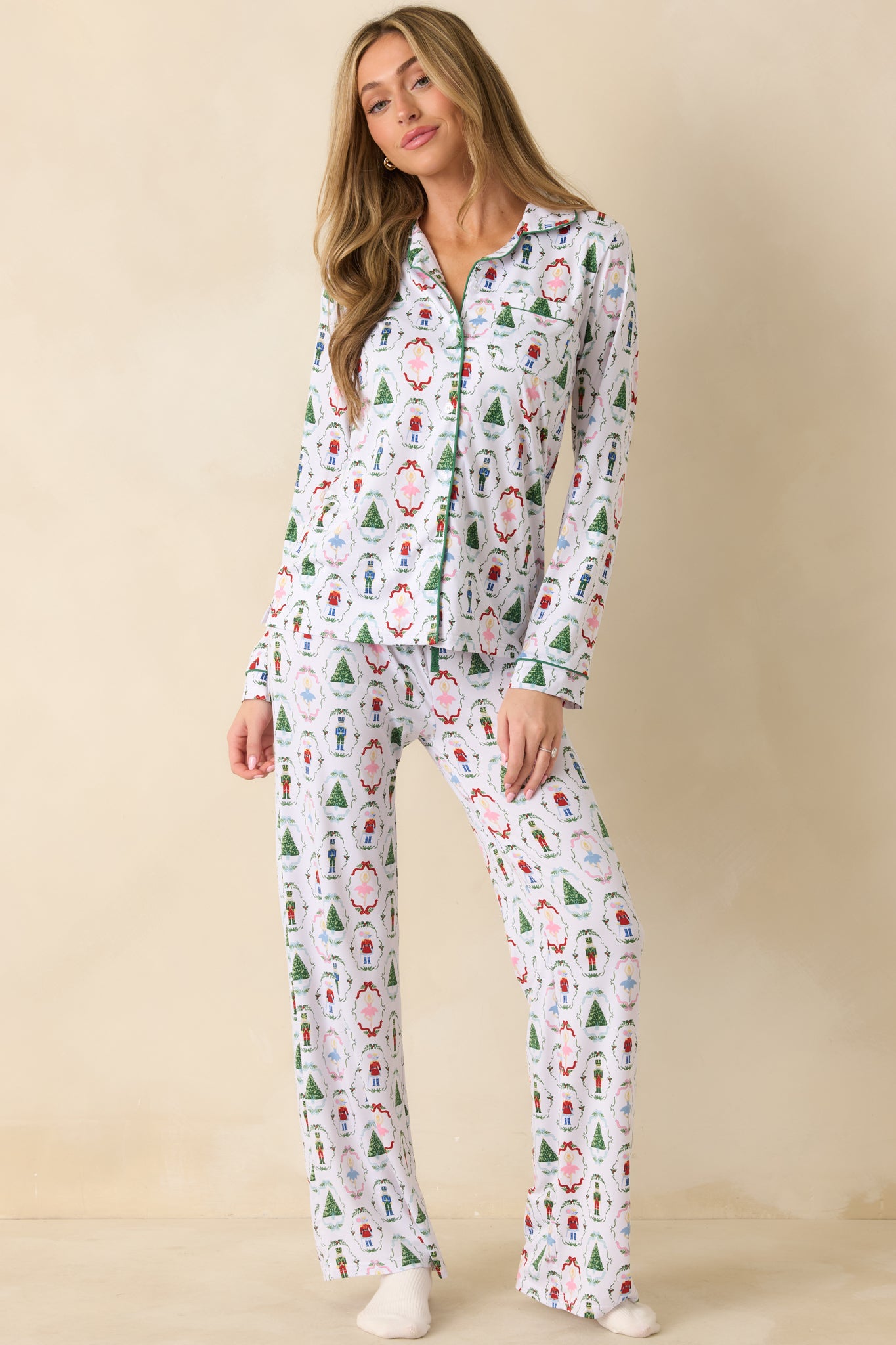 Front view of the white pajama pants showing the nutcracker and holiday motif print with green piping and a relaxed wide-leg fit.