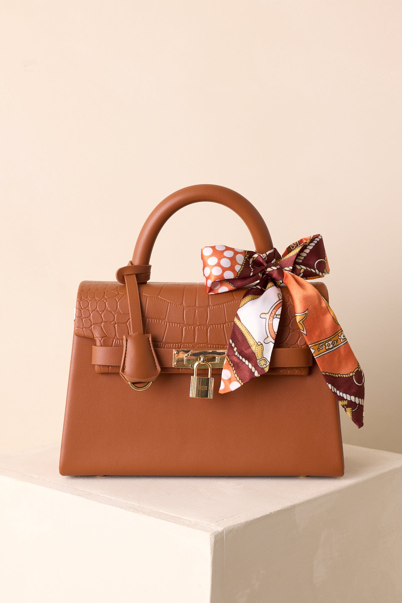 A full front view of the brown structured handbag with tan faux leather, padlock closure, and decorative self-tie scarf.