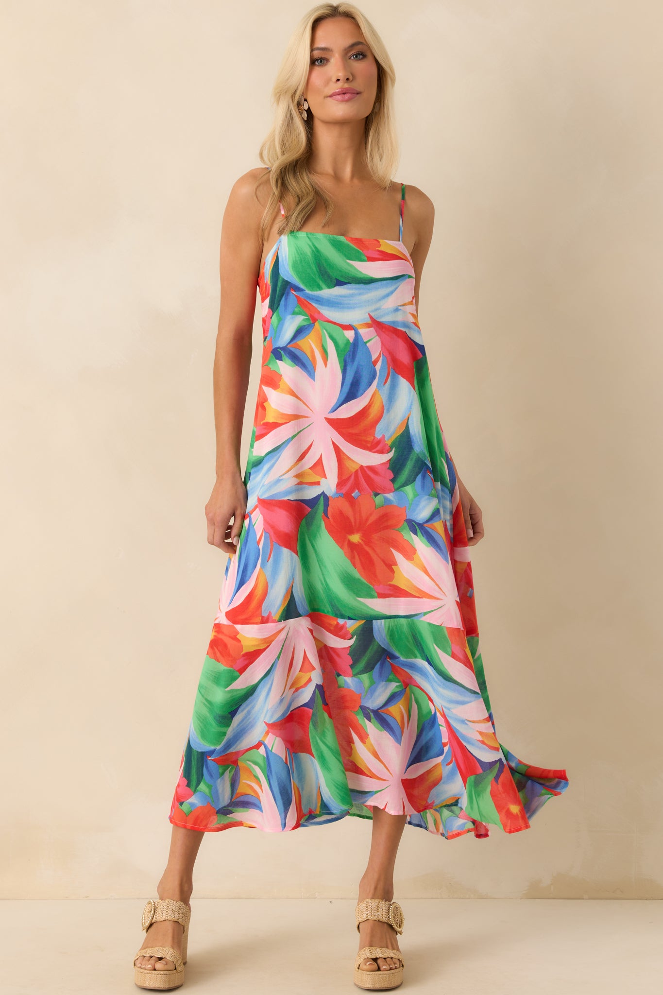 Straight-on full body image highlighting the maxi dress’s bold pink tropical floral print and the structured square neckline framed by self-tie straps.