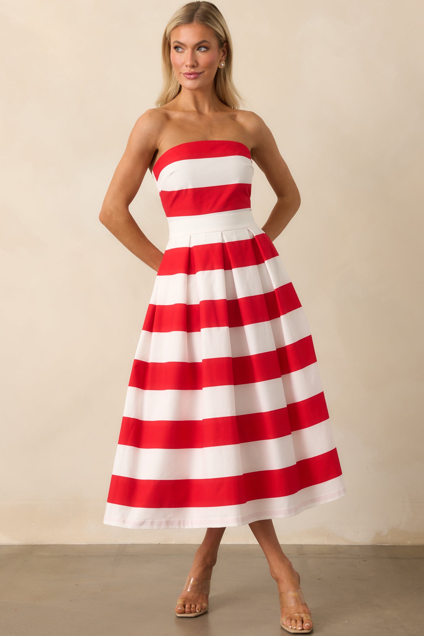 A full-length view of the red and white striped dress shown with subtle pleats in the skirt and features functional side pockets.