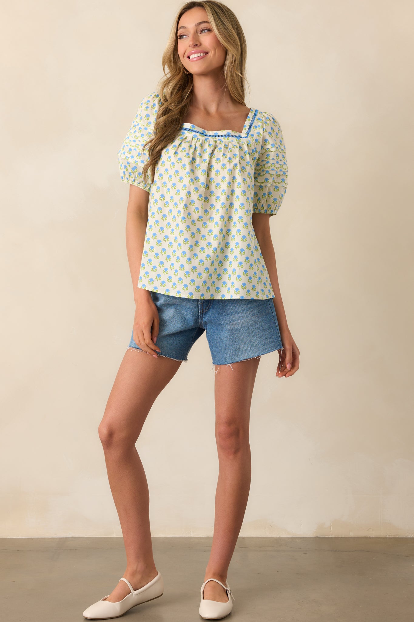 Front-facing full shot of a floral cotton blouse featuring ladder lace trim and short puff sleeves.