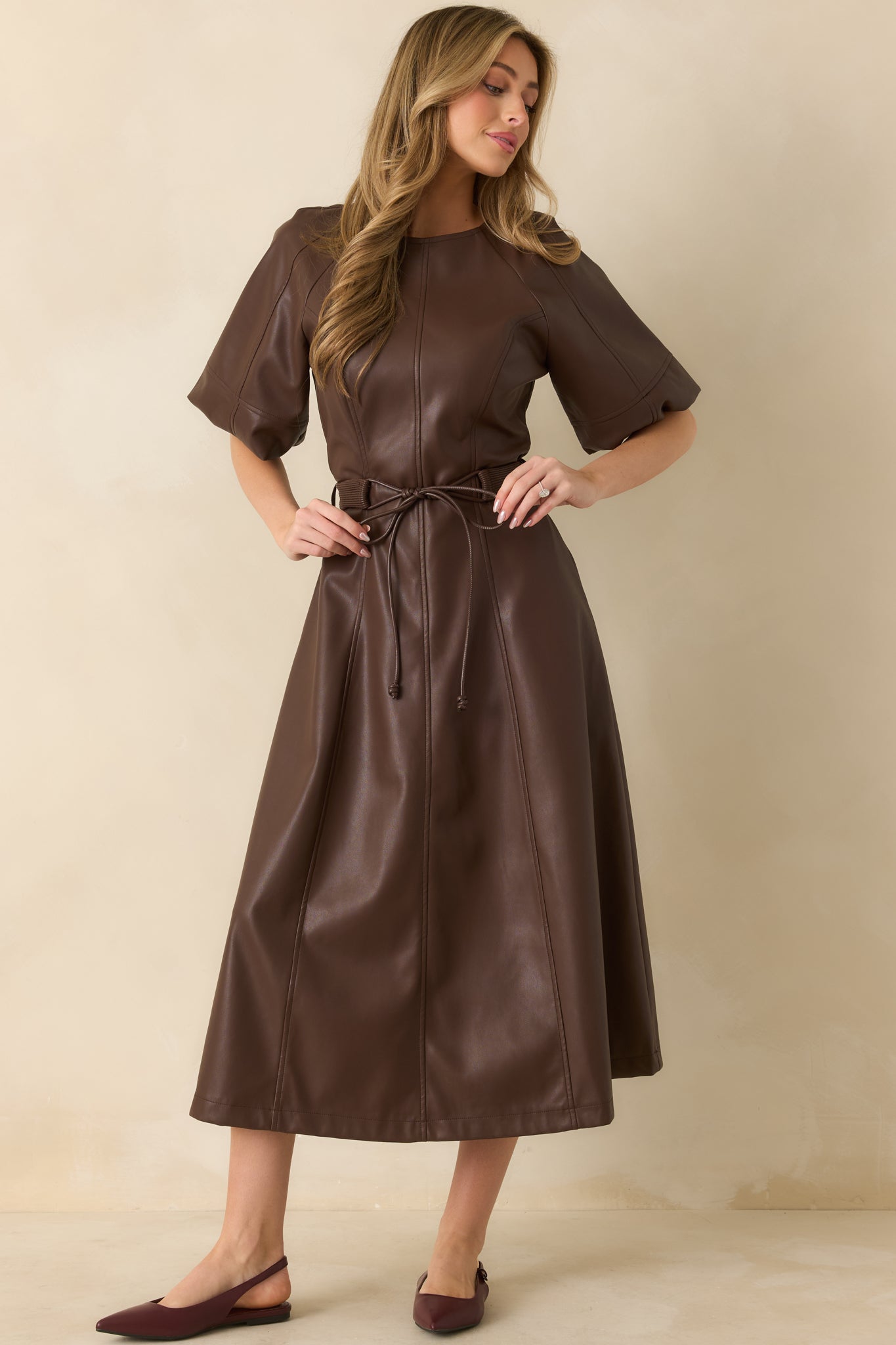 Full-body shot of the brown faux leather midi dress showing short raglan sleeves, crew neckline, and adjustable waist tie.