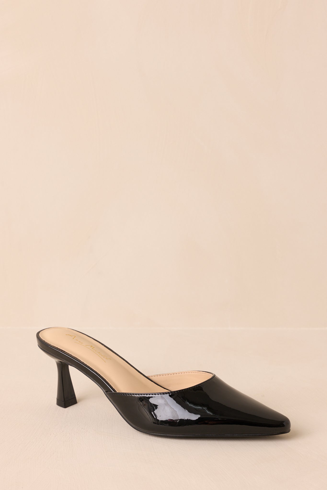 A full side angle of the black mule against beige background, showing the slip-on design and kitten heel.
