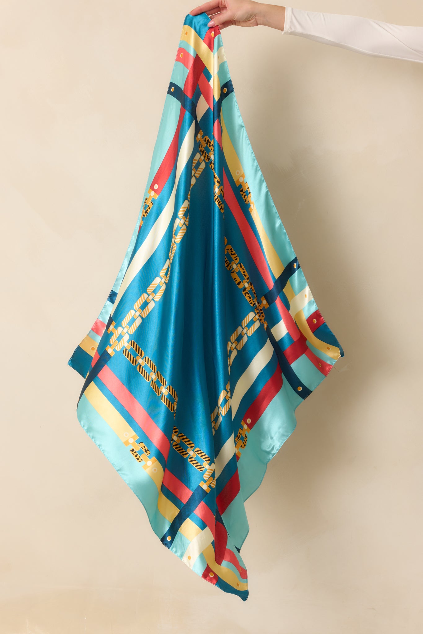 Full view of the blue satin scarf featuring a vibrant multi-color chain print with gold, pink, yellow, teal, and blue accents along the edges.