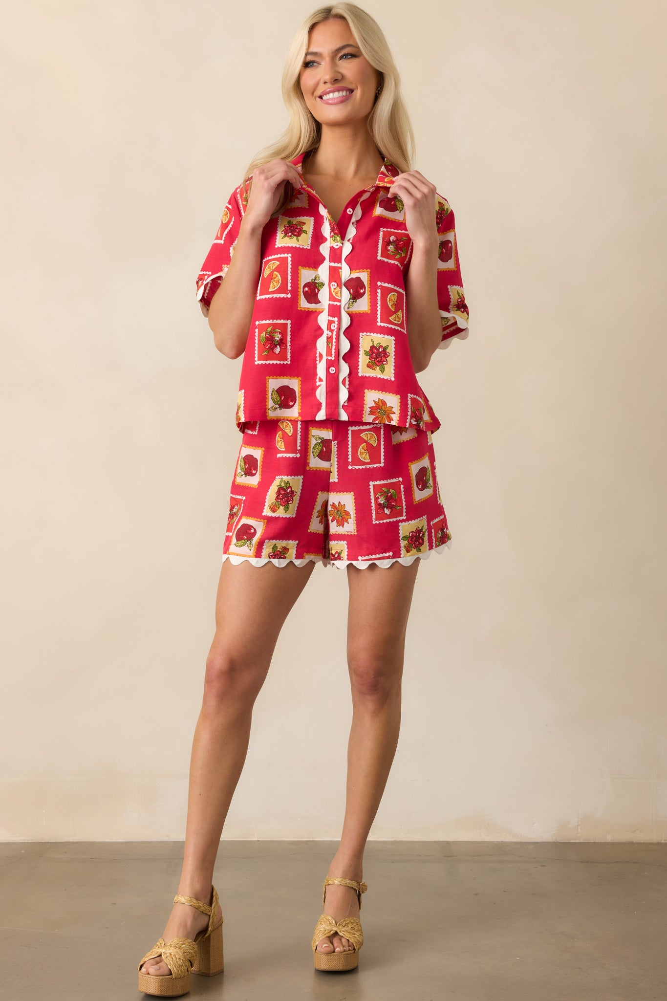 Full body view of a red top with a stamp-inspired patchwork print and floral and fruit motifs, featuring a relaxed fit and collared neckline.