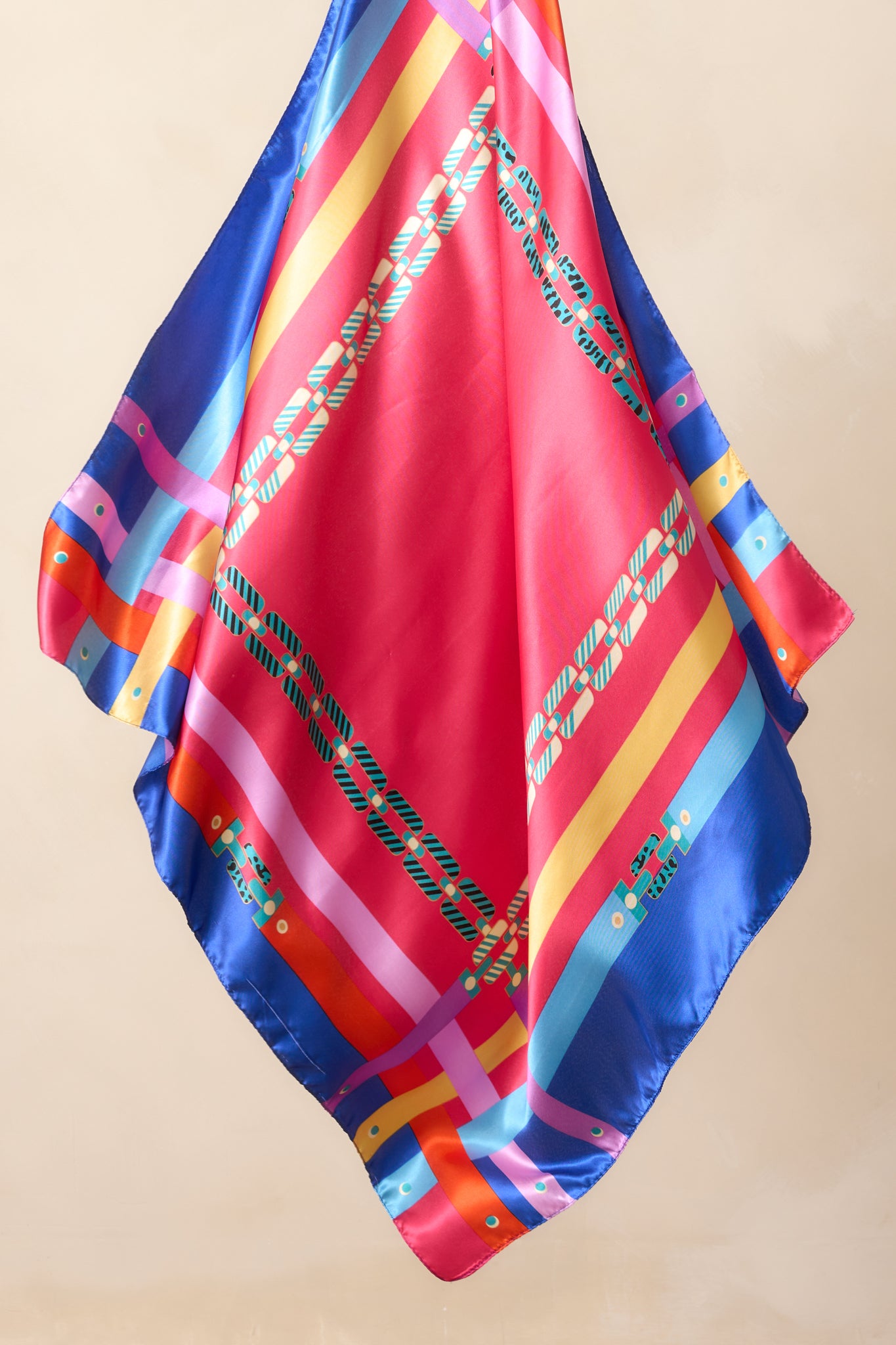 Full view of the fuchsia satin scarf featuring a vibrant multi-color chain print with purple, orange, yellow, teal, and blue accents along the edges.