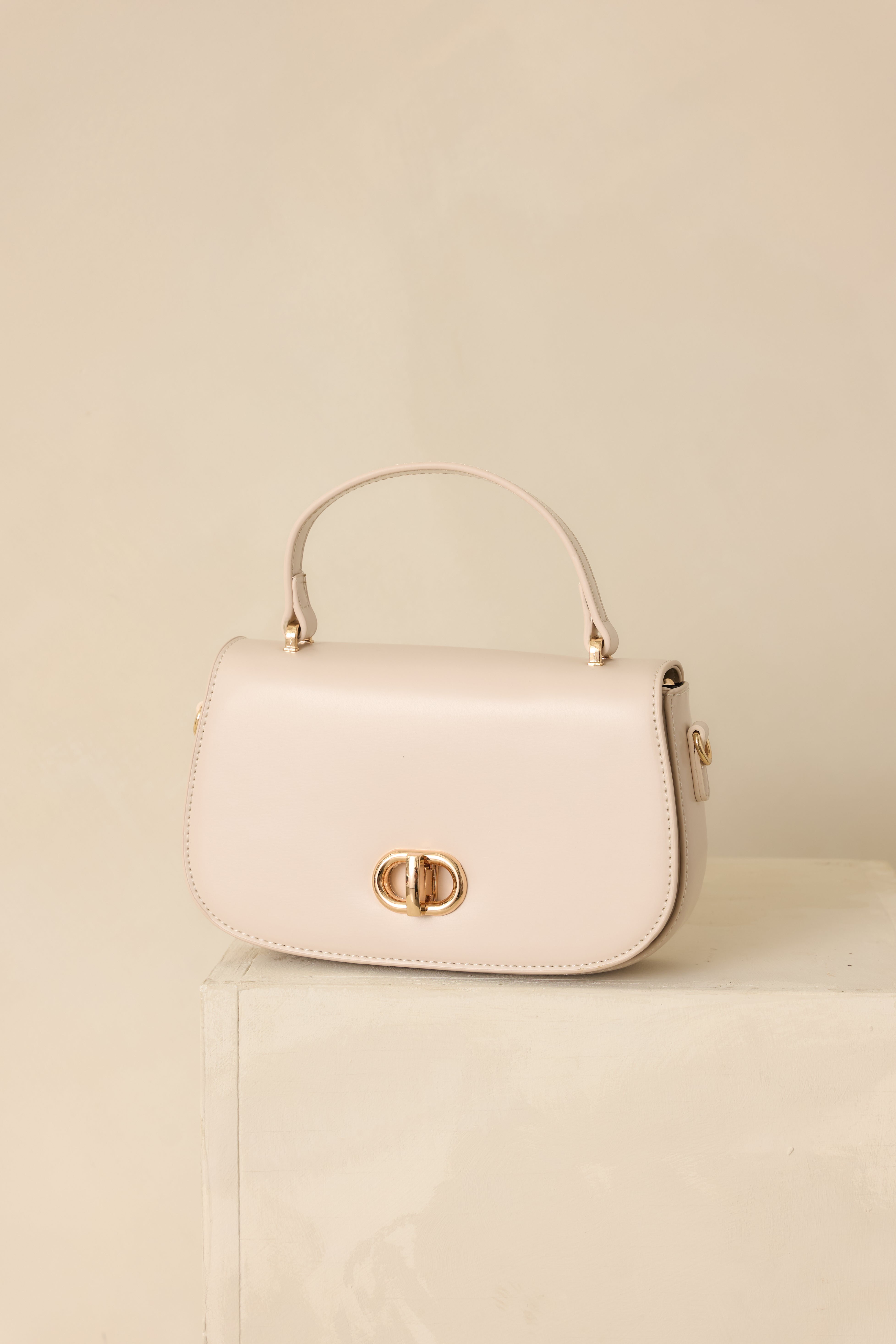 A full view of the ivory structured handbag with a flap closure, gold turn-lock detail, and single top handle.
