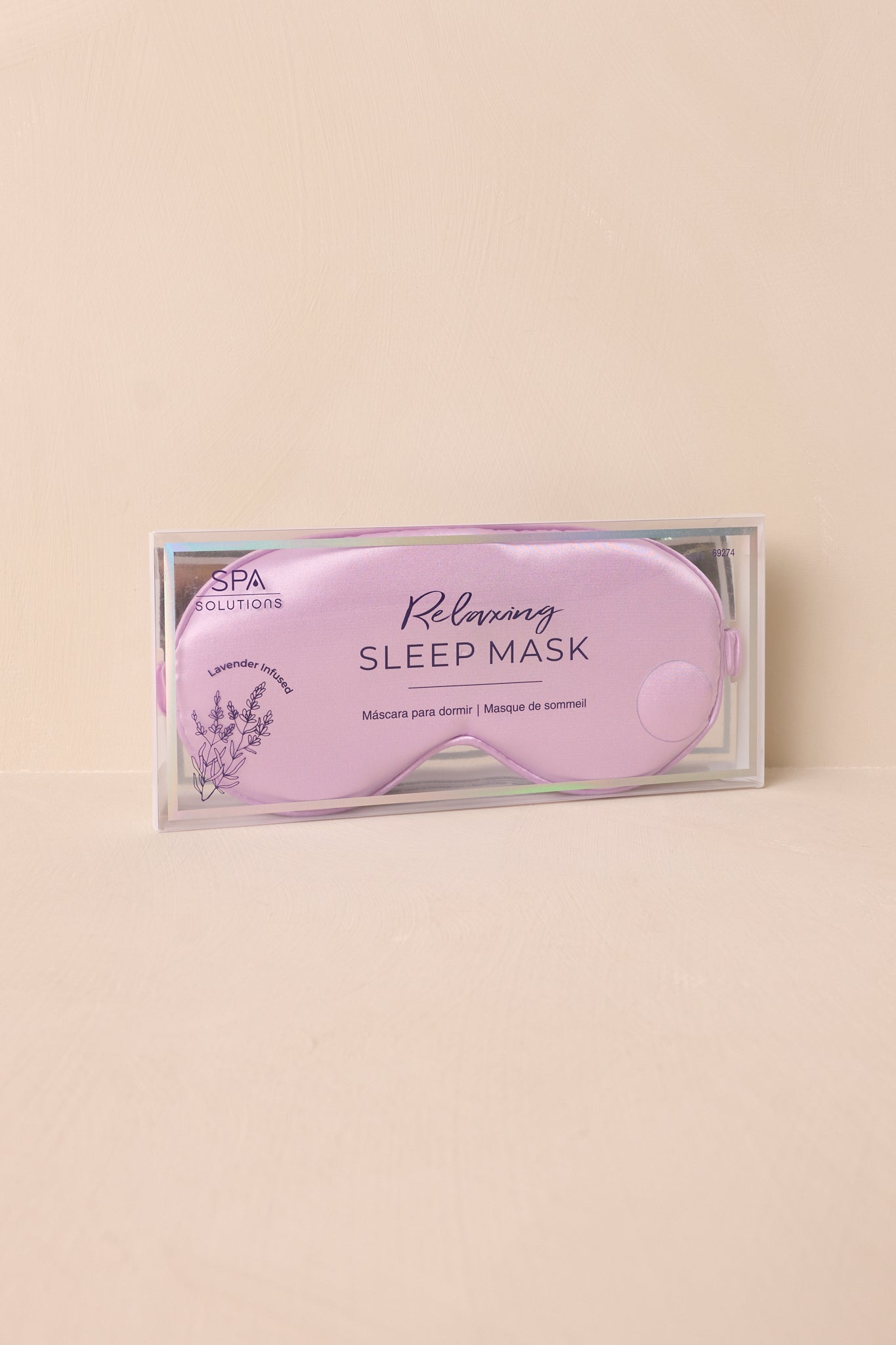 A full view of the eye mask lying flat on a beige surface, showing its contoured shape and light-blocking design.