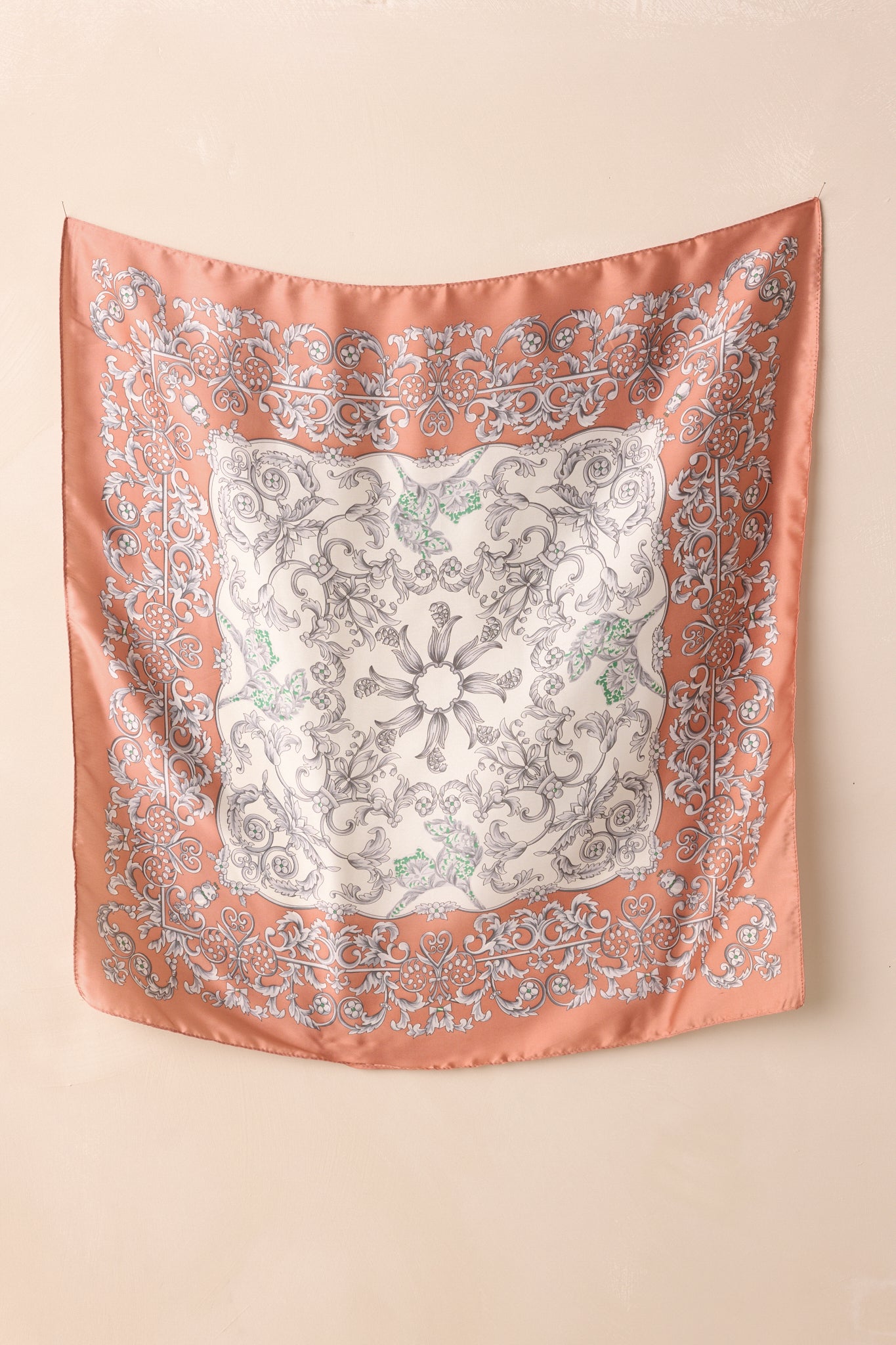 Full view of the square scarf featuring a rose pink border with ornate grey scrollwork and floral motif, accented with subtle green details.