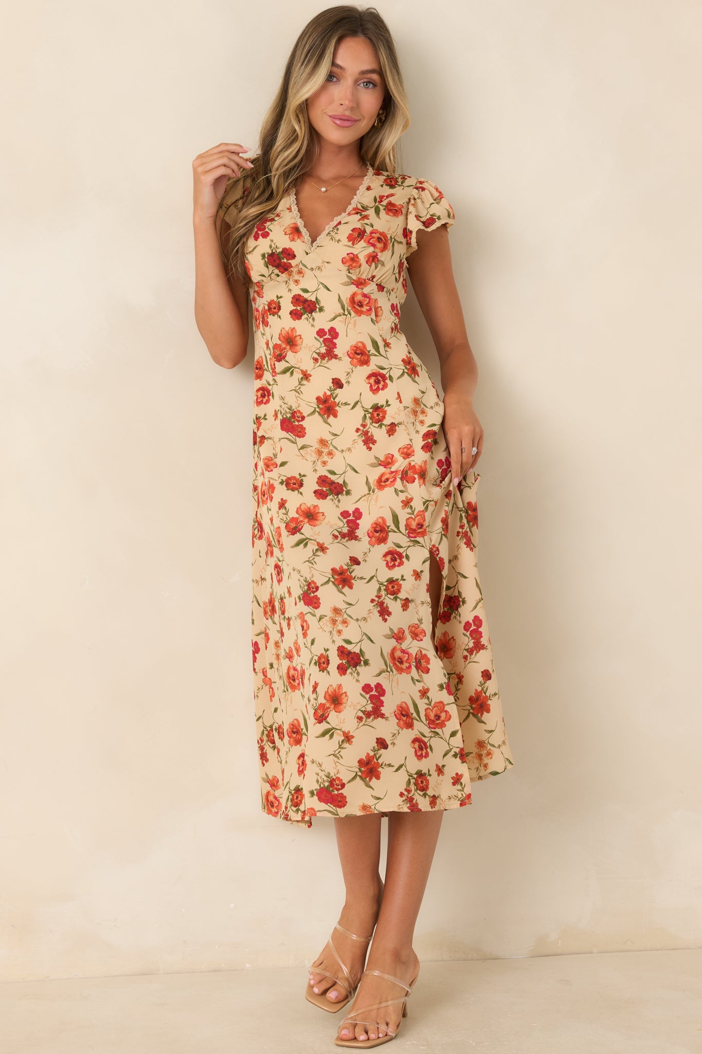 Garden floral midi dress showcasing a light beige base, red and coral blooms, flutter sleeves, side slit, and flowing silhouette.