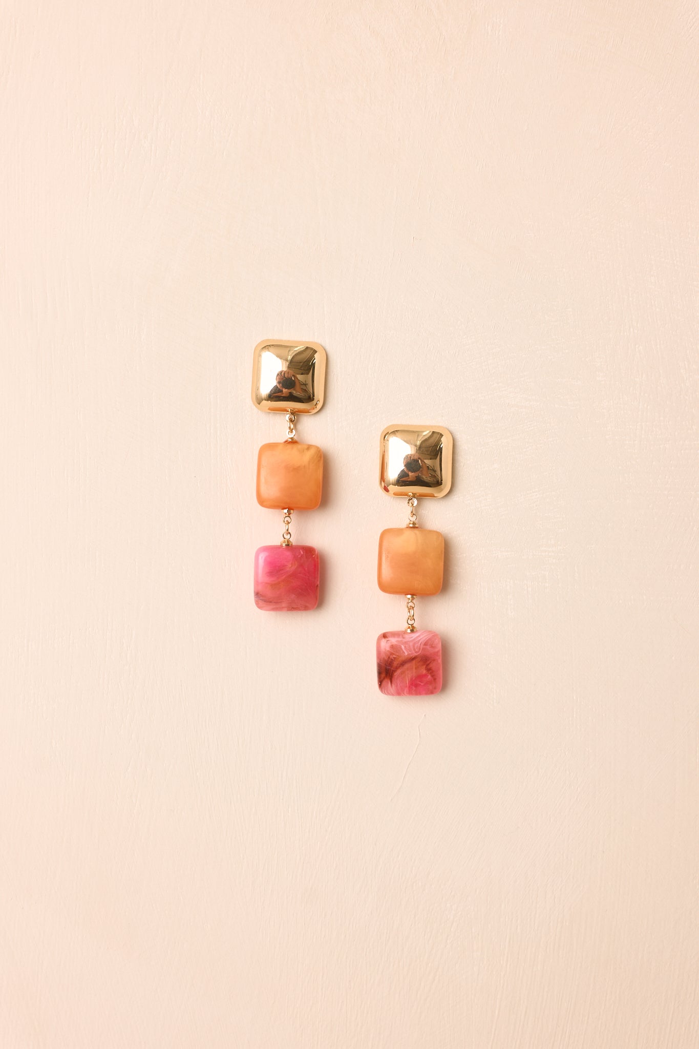 Front view of orange and pink square earrings displayed on beige background emphasizing bold geometric design.