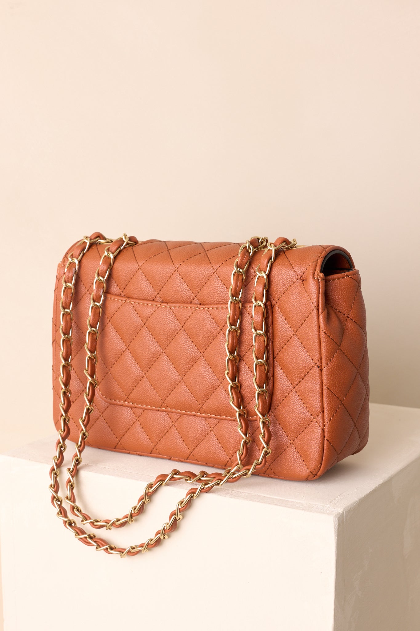 Ginger brown quilted handbag with exterior slip pocket on the rear side.