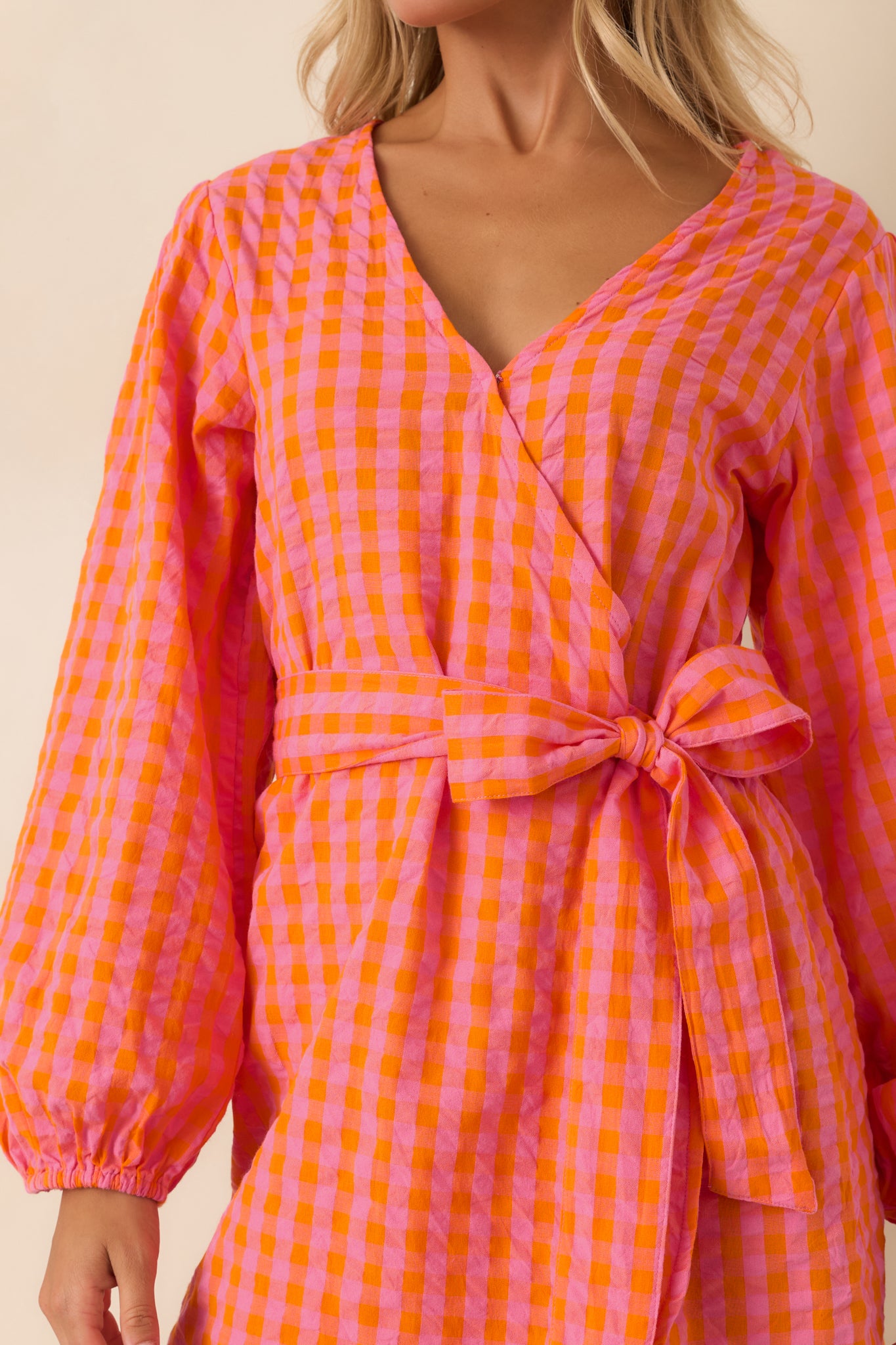Detailed view of the pink and orange gingham fabric, wrap construction, self-tie waist, and lightweight cotton texture.