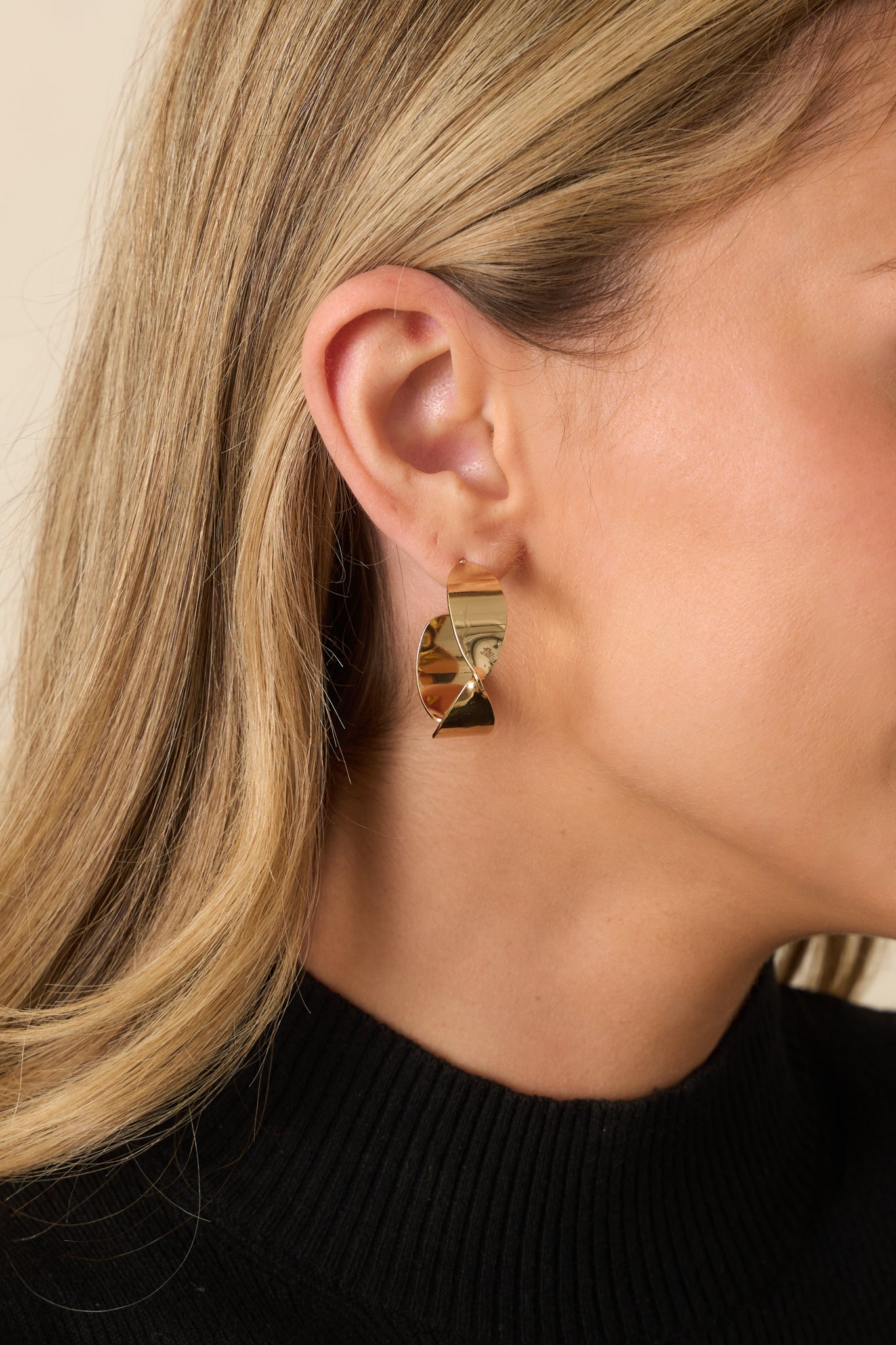 A cropped front view showing the polished gold abstract twisted hoop earrings with post back closure.