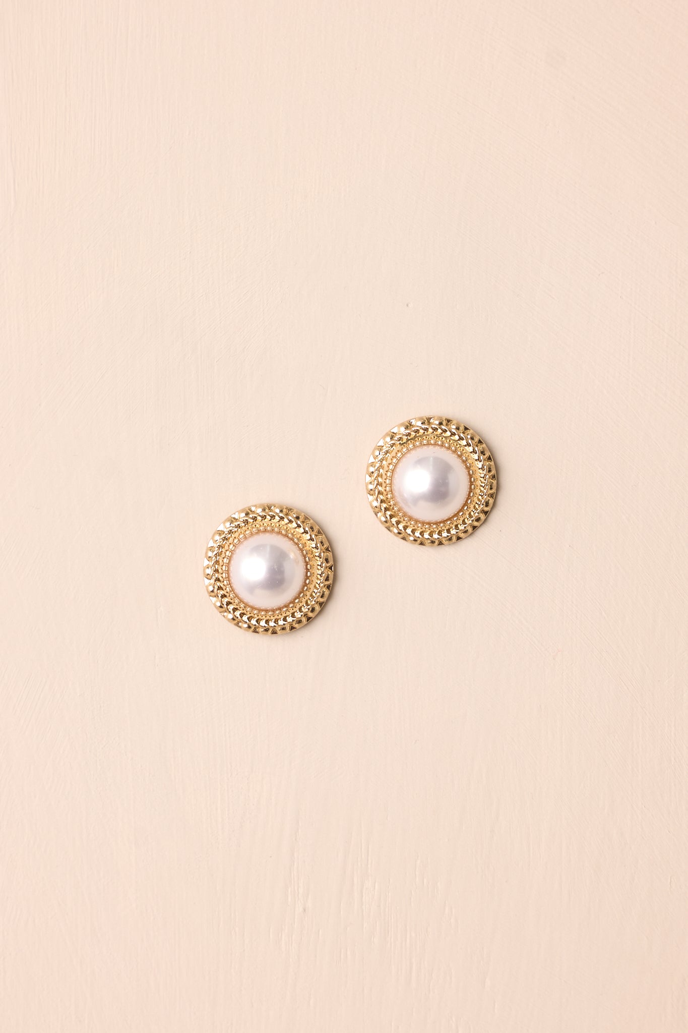 A pair of gold and ivory earrings with gold hardware, featuring a stud design with a large circular shape and a central ivory pearl surrounded by a thick textured gold border.