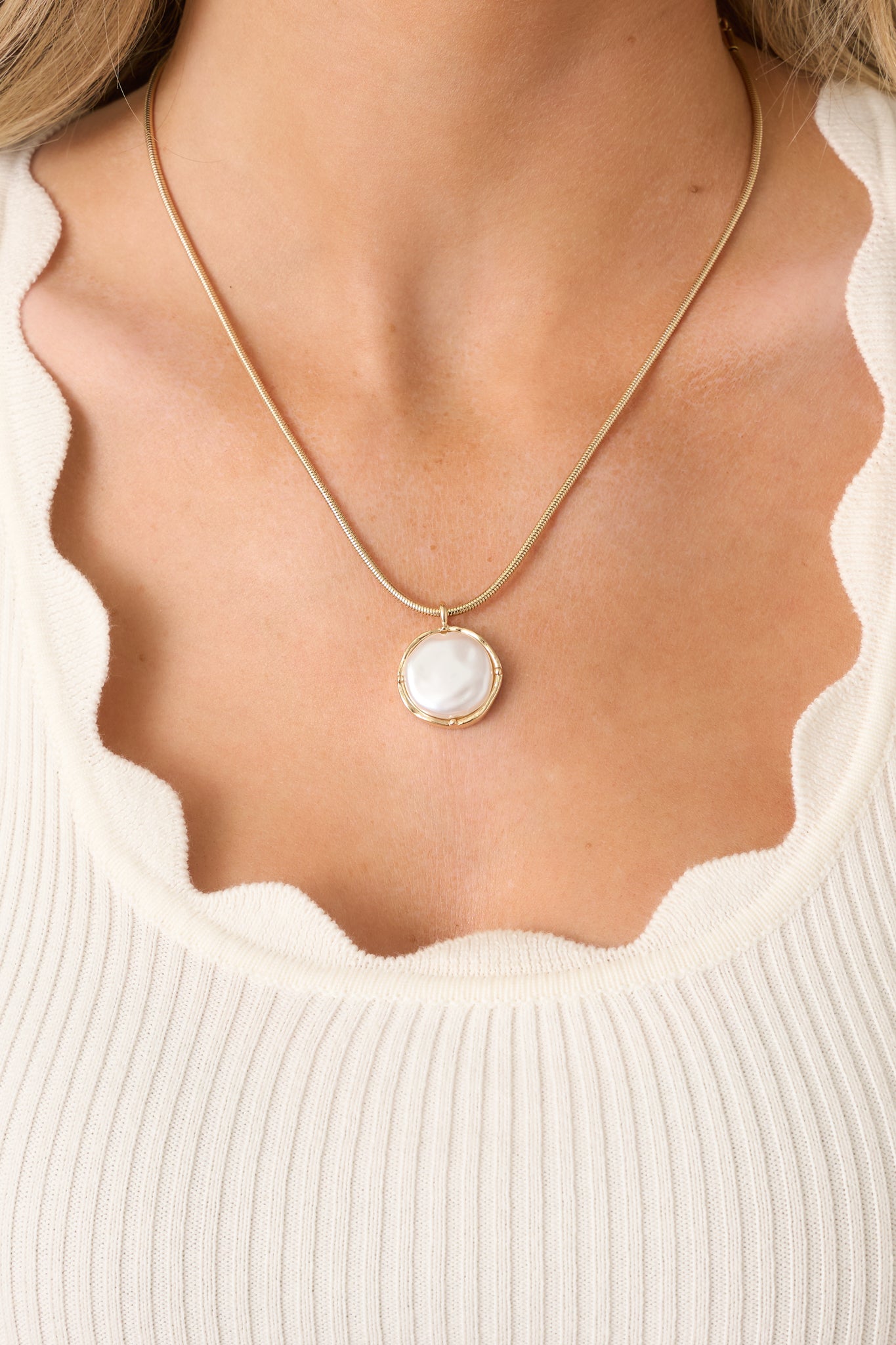 Close-up of gold and pearl pendant showing luminous pearl encased in sleek gold frame and attached to fine gold chain.