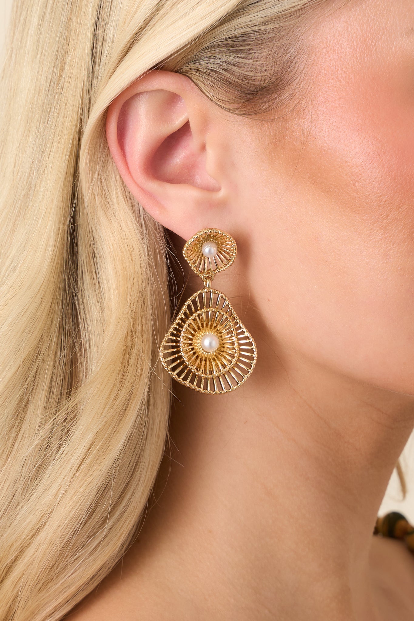 Close-up of gold and pearl statement earrings showing intricate layered sunburst design and luminous pearl details.