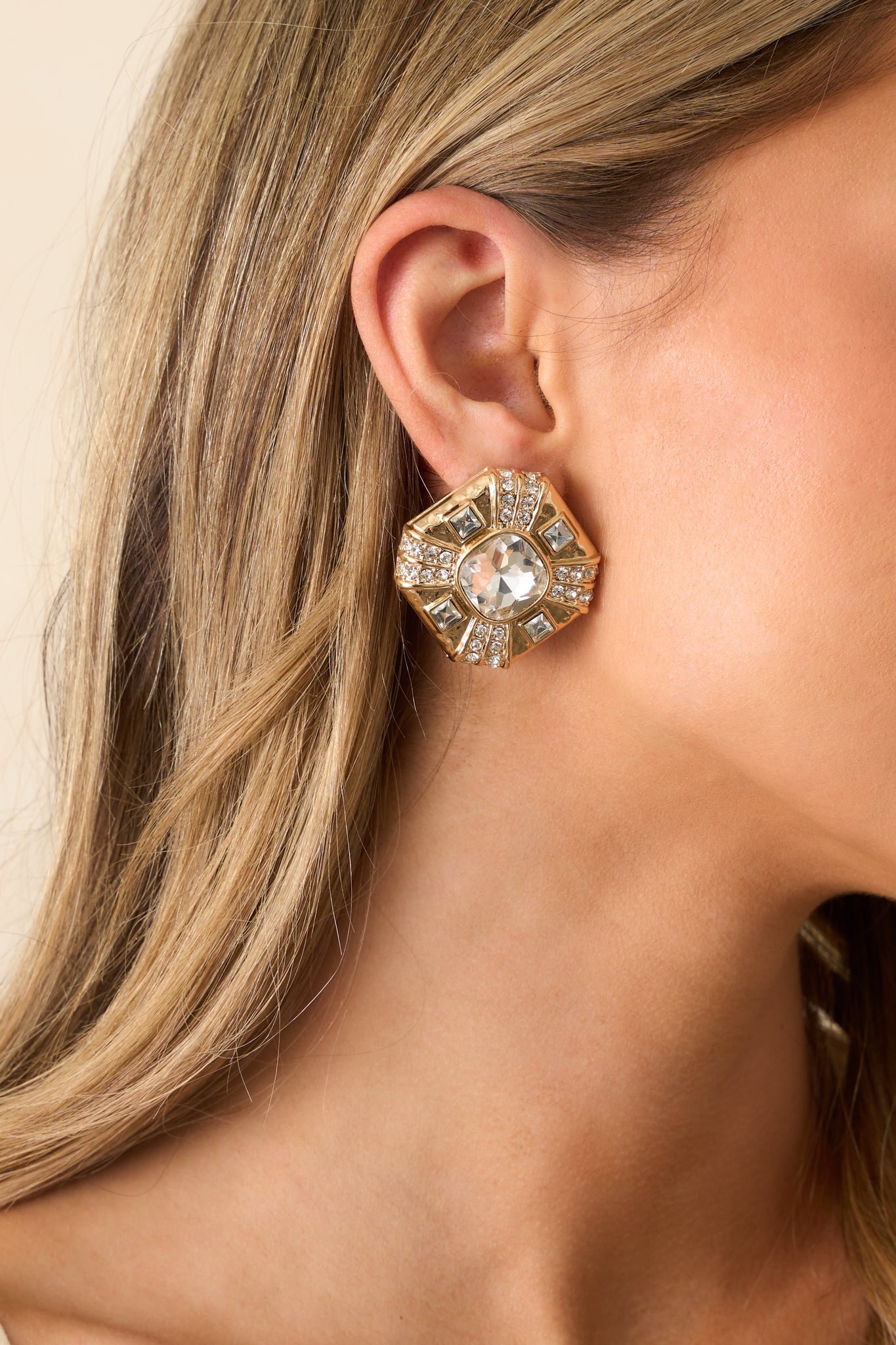 A partial view of the gold and rhinestone earrings, highlighting the rounded square shape and sparkling rhinestone details.