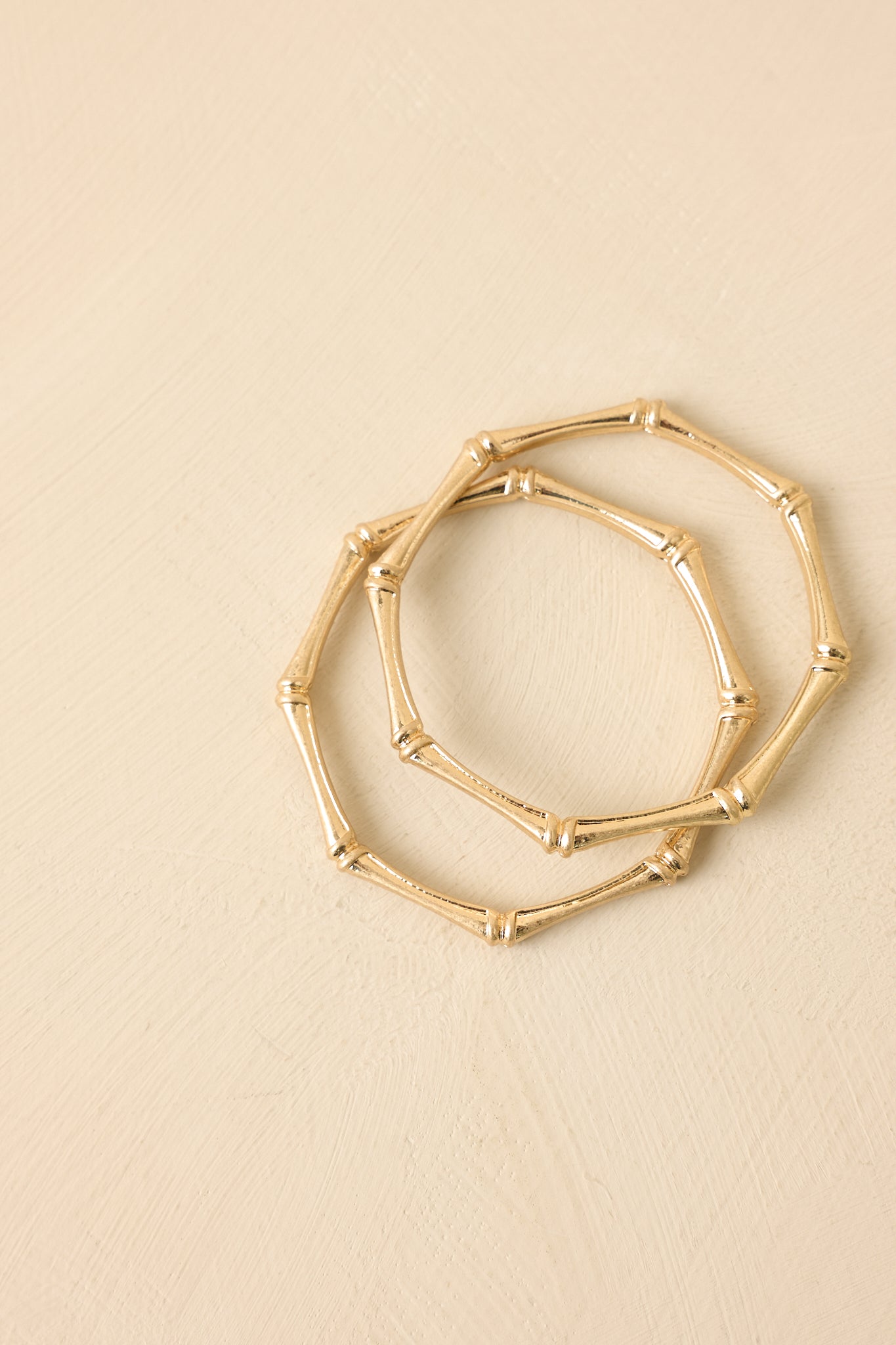 Gold bamboo bangle bracelet set displayed on a beige background, emphasizing textured surface and clean, classic silhouette.