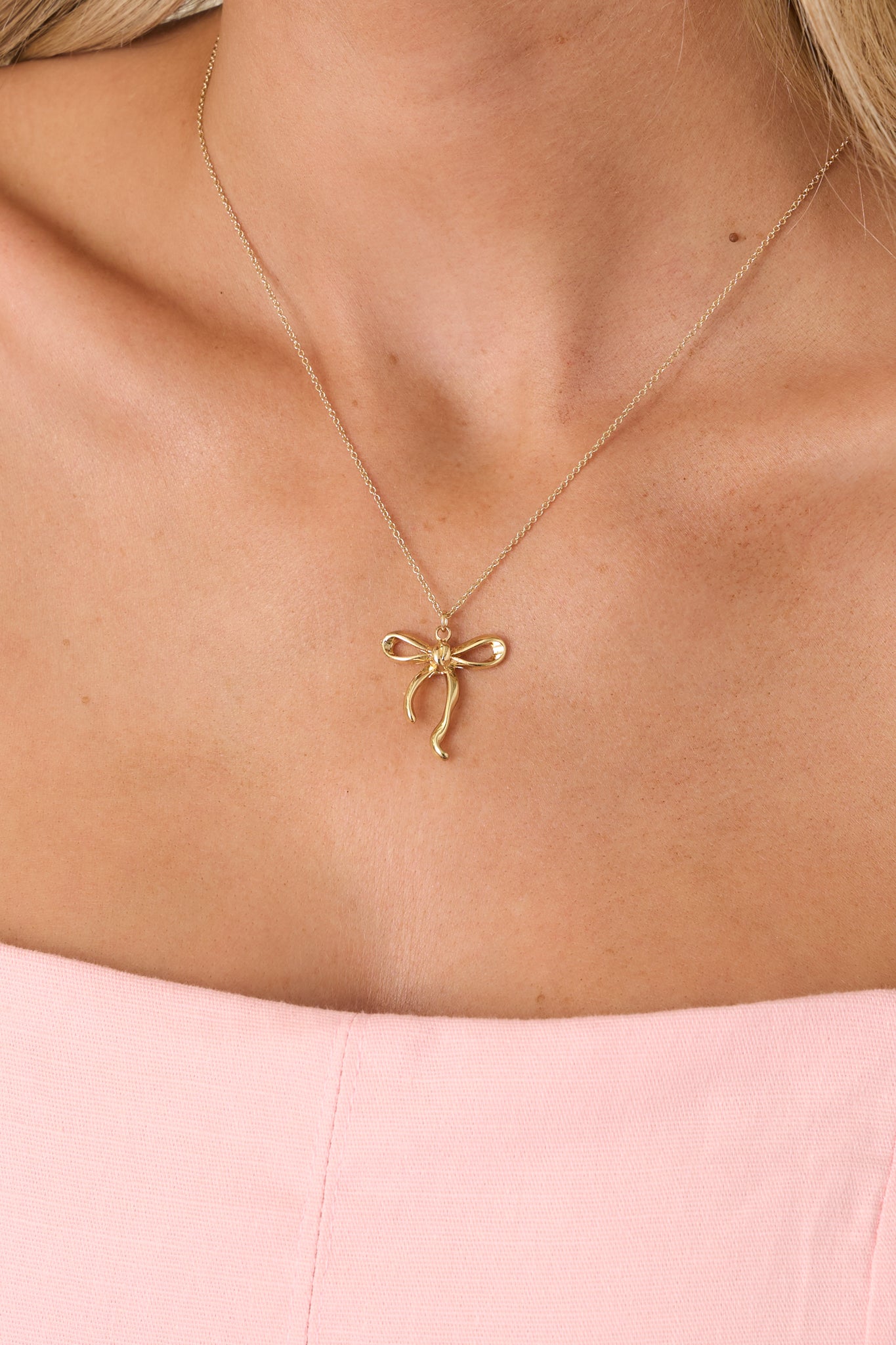Close-up of the gold bow pendant and fine chain, emphasizing the smooth polished finish and elegant sculpted details.