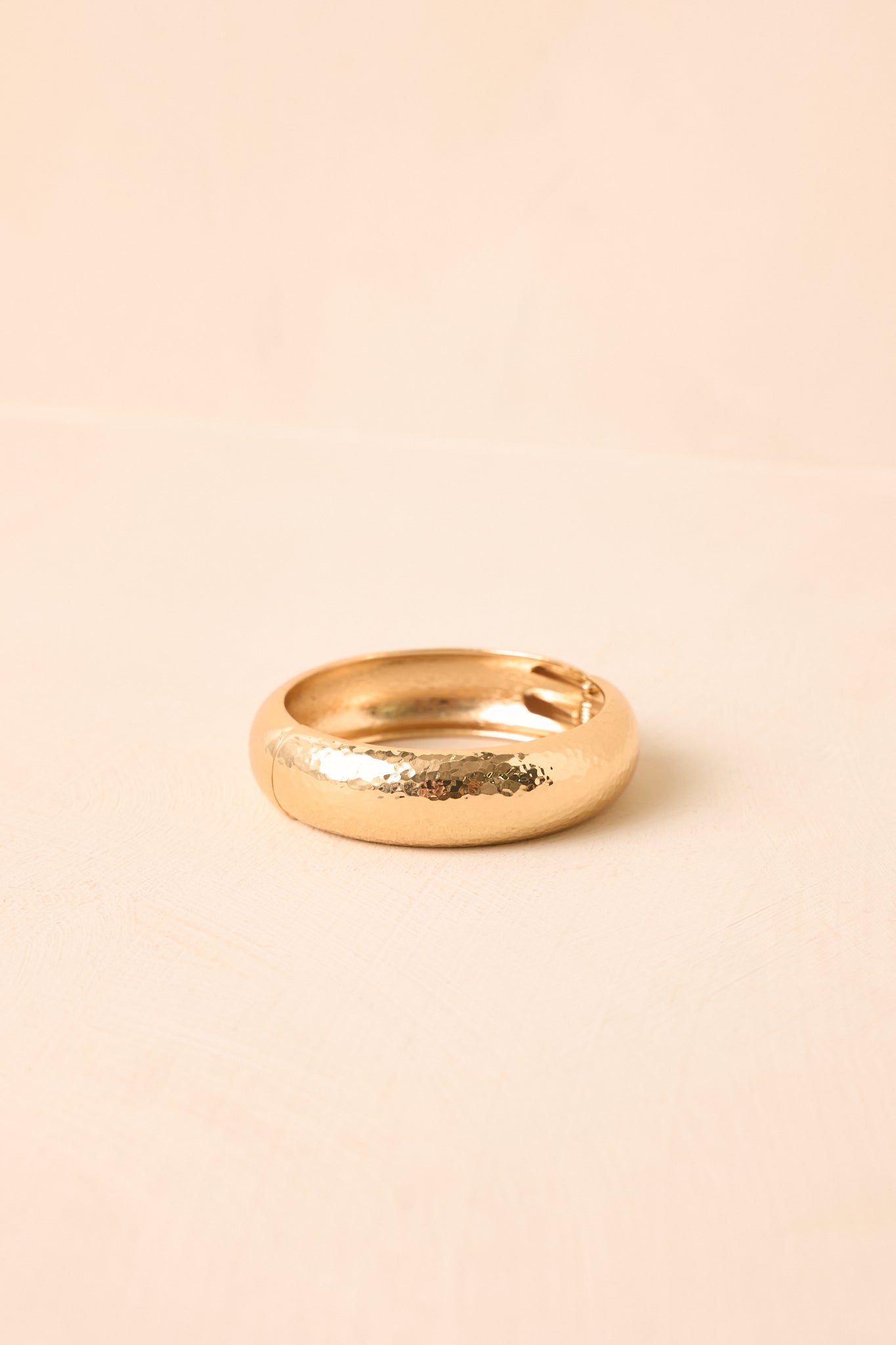 Gold bracelet with an organic hammered finish presented on a neutral backdrop, emphasizing its statement design.