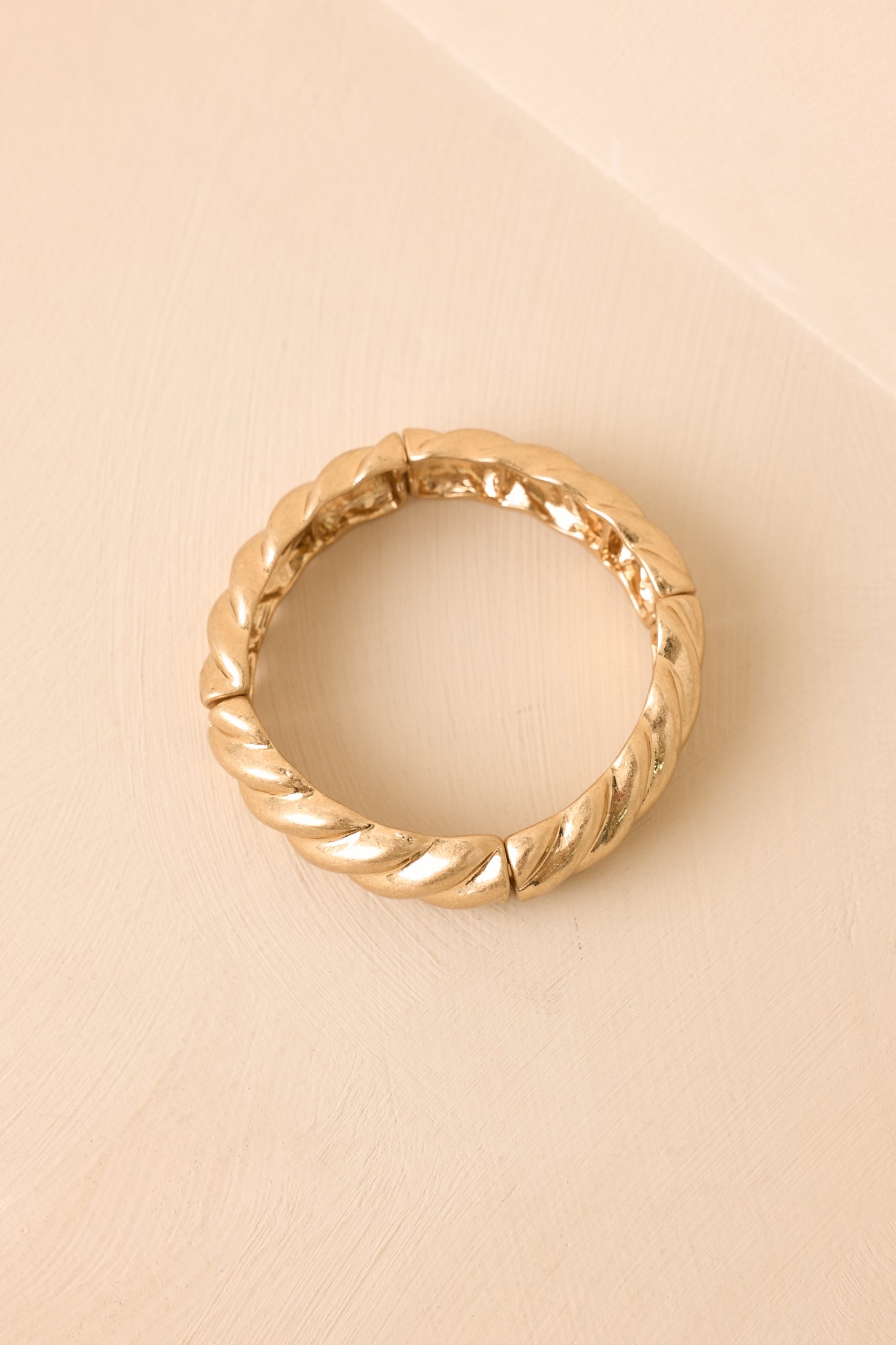 Gold bracelet showcasing polished twist links and a softly textured metallic finish against a beige background.