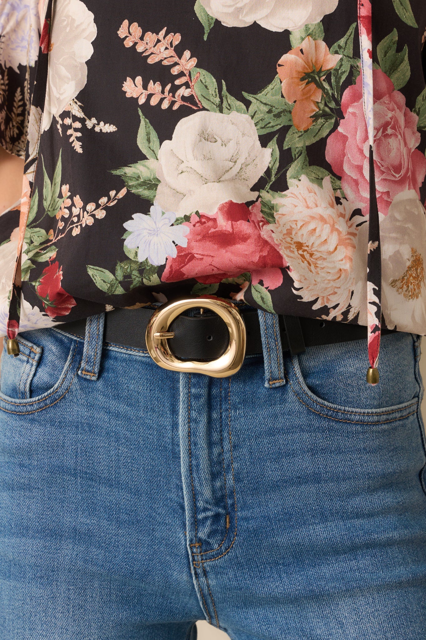 A close-up of the gold buckle with its hollow organic design and polished finish against the faux leather strap.