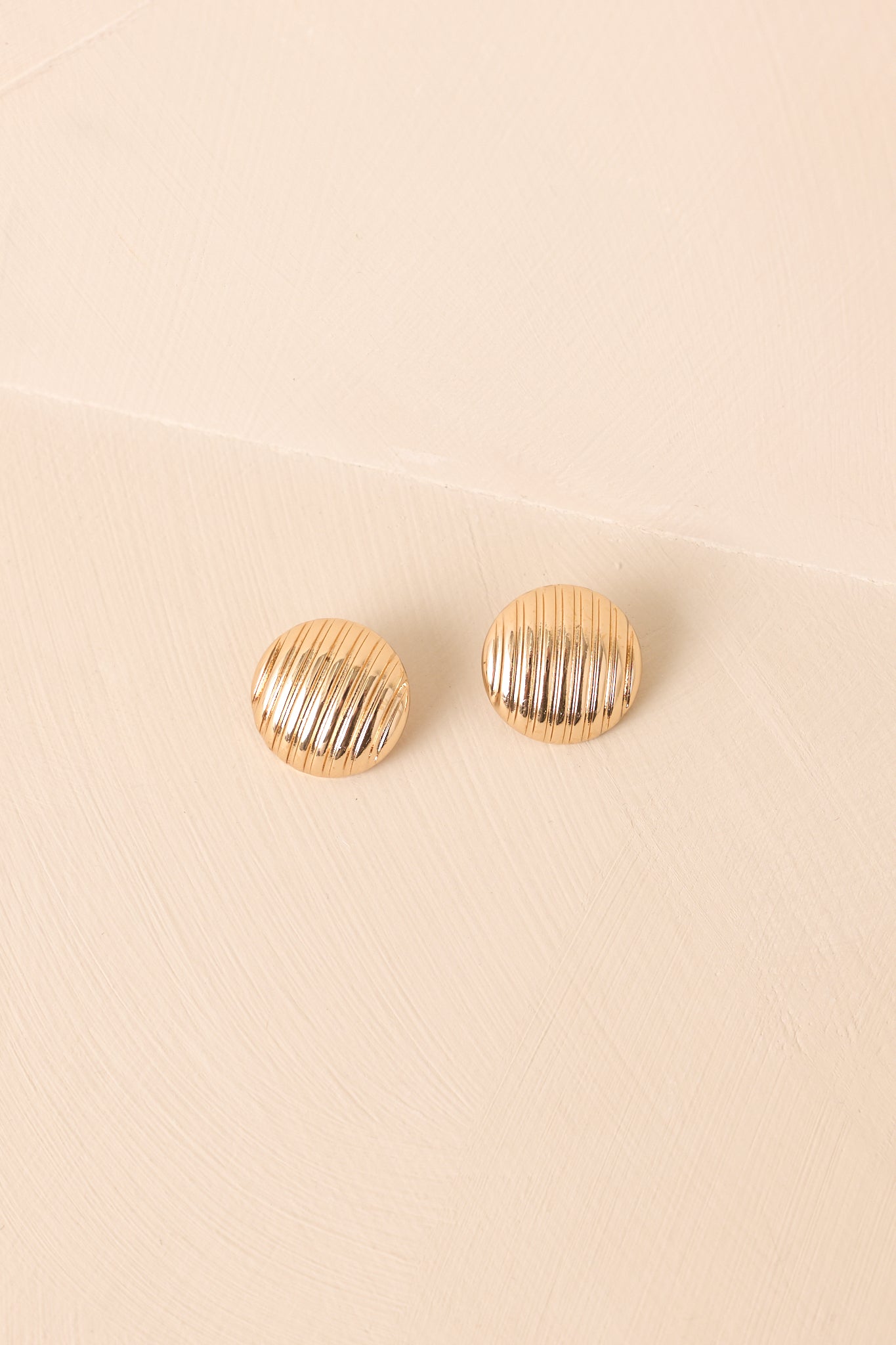 Gold circular earrings displayed against a beige background, emphasizing the ribbed design and polished finish.