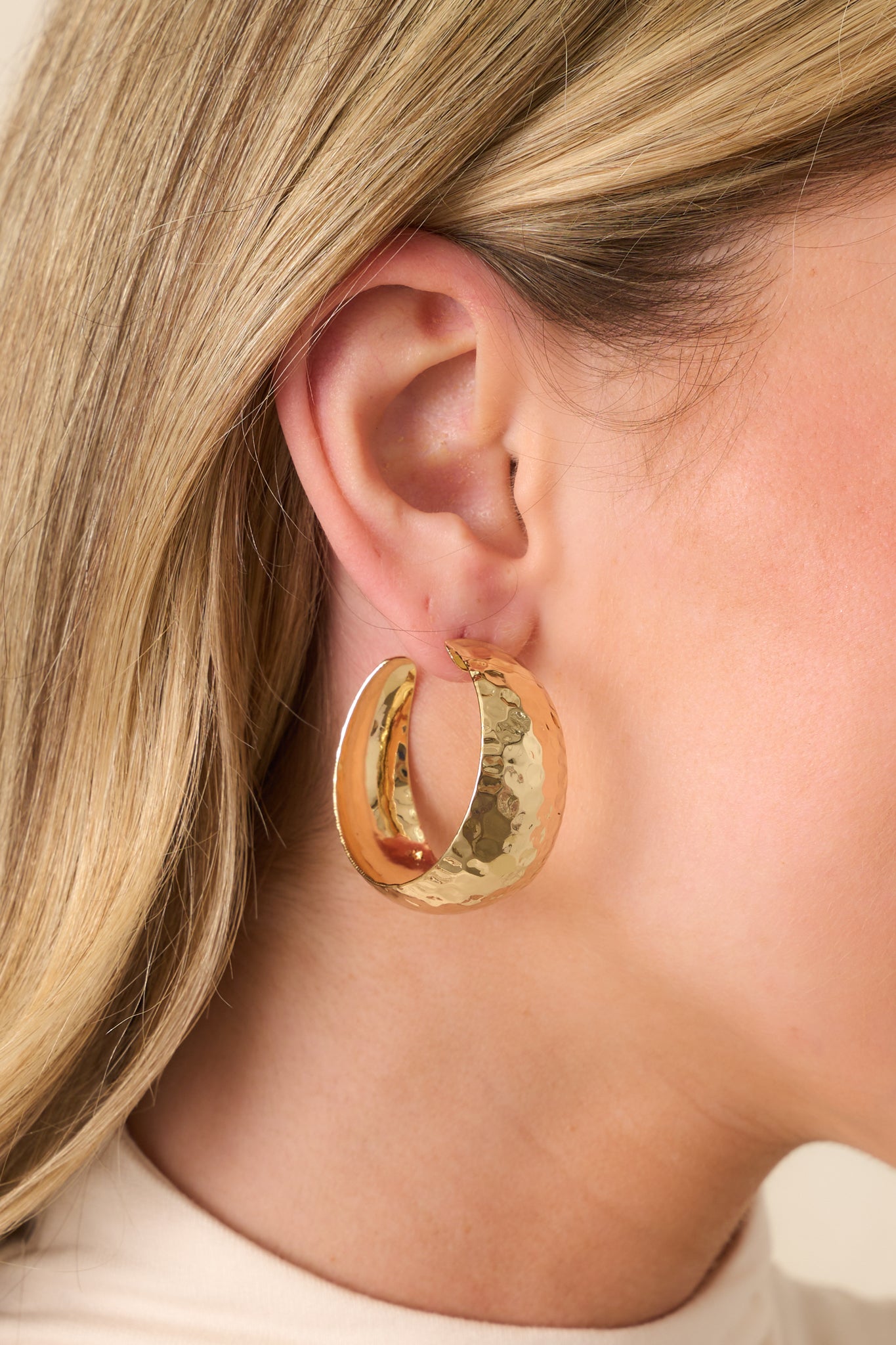 A close-up of one gold earring showing the hammered textured finish and secure post backing in fine detail.