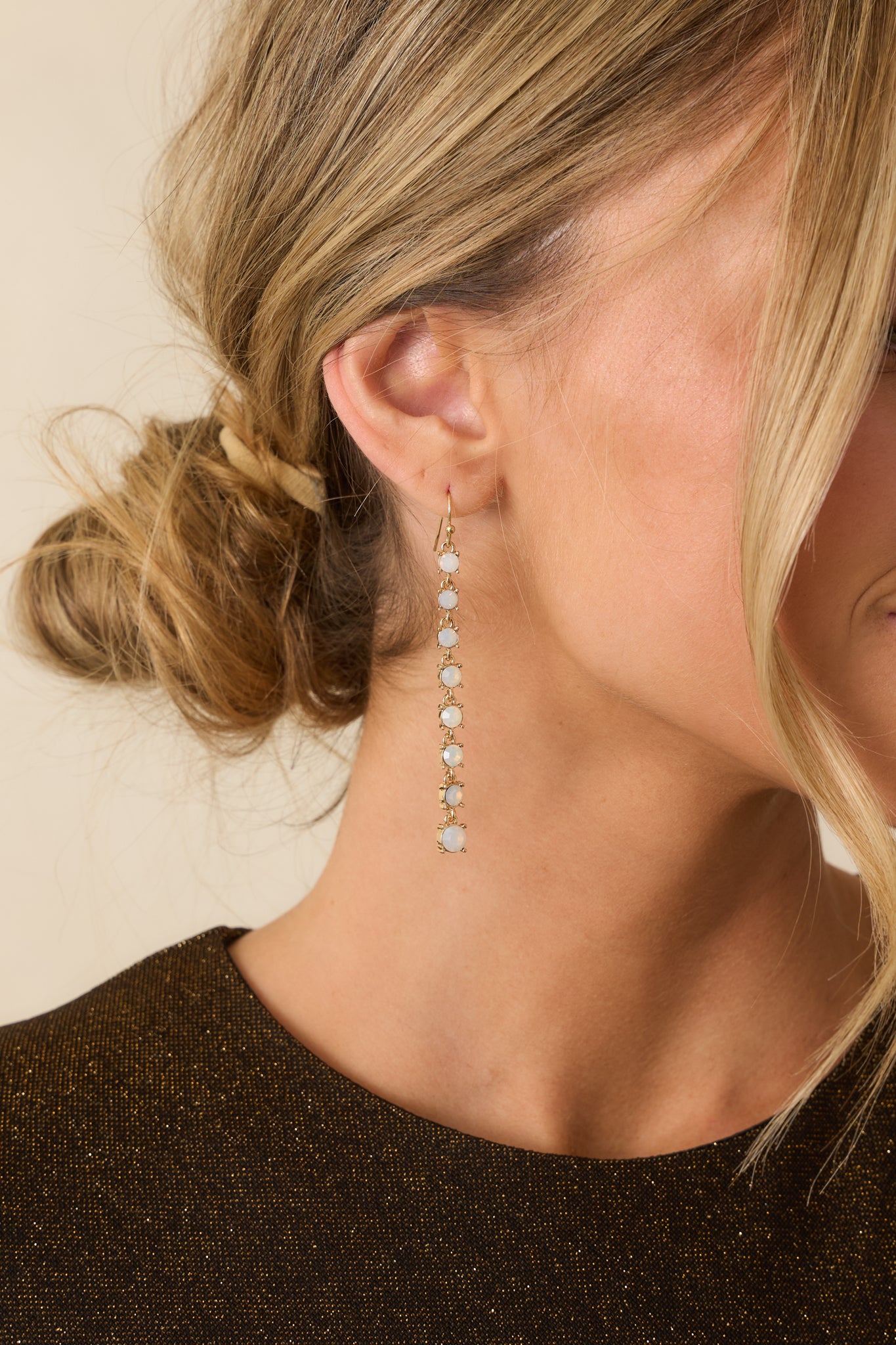 Cropped view of gold drop earrings featuring a vertical line of faux opal stones set in gold-tone metal.