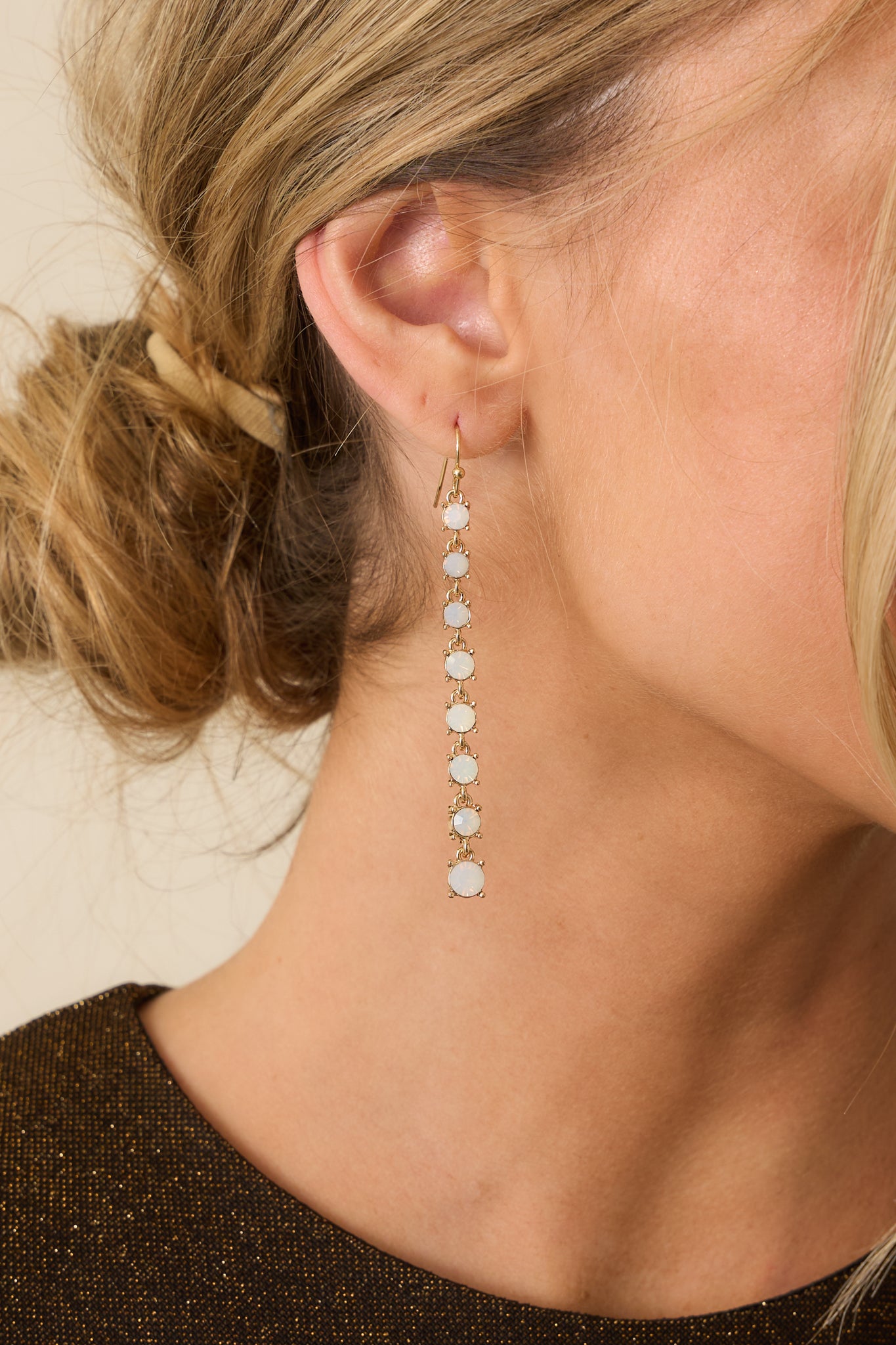 Close-up of one gold drop earring showing the opal stone textures, gold-tone settings, and curved fish hook backing.