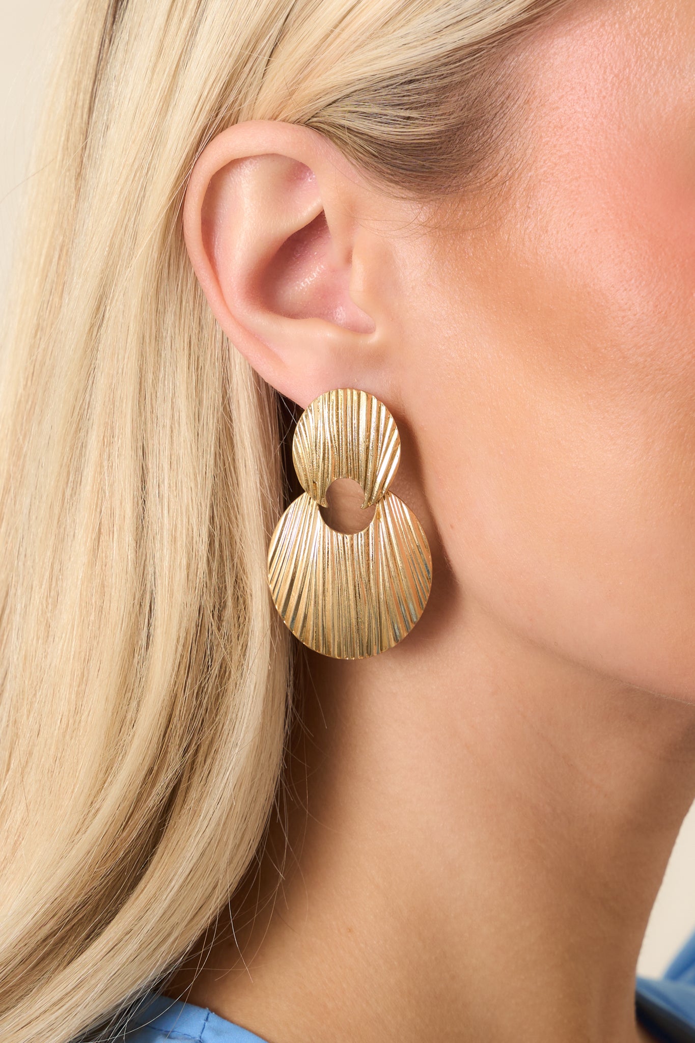 Close-up of gold drop earrings showing intricate ridged texture on layered oval discs for a polished, modern look.