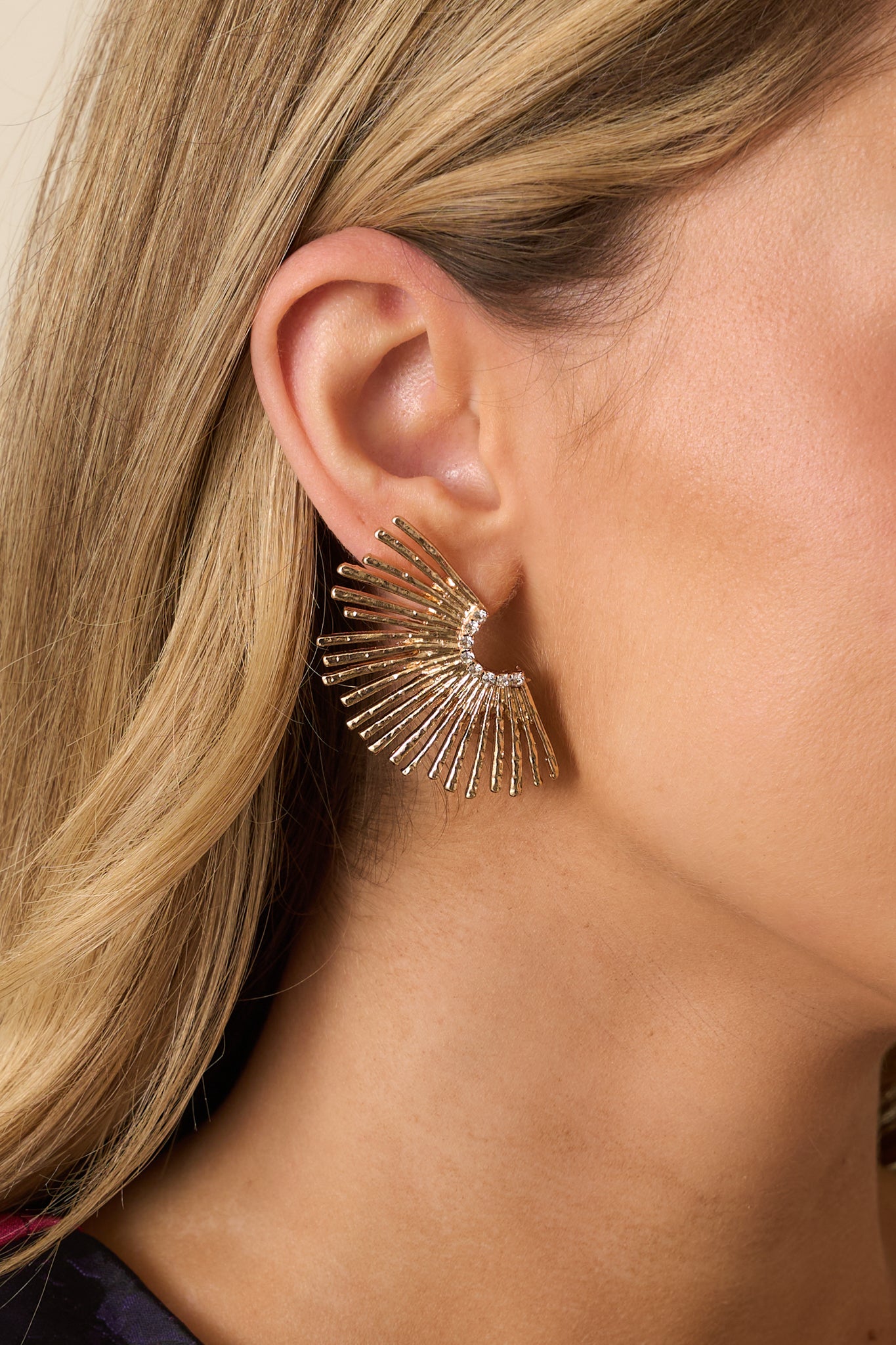 Extreme close-up of one gold earring showing intricate fan etching, rhinestone accents, and post backing detail.