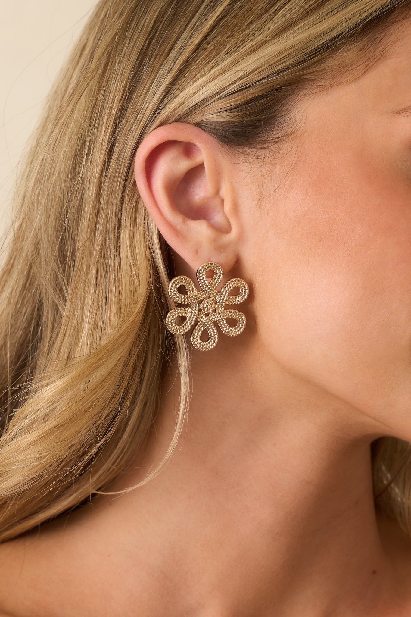 A cropped front view of the gold earrings showing an open-petal flower design with textured beading and central floral cluster.