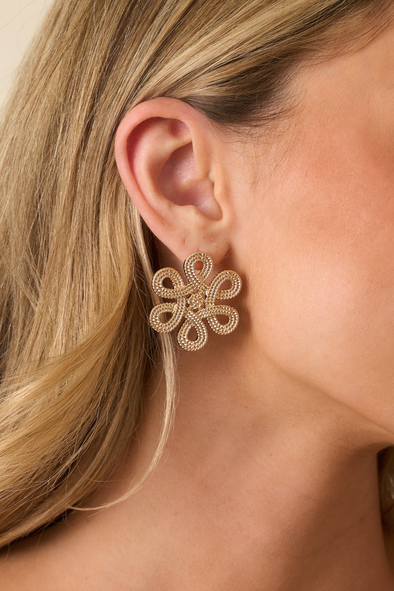 Gold open-petal flower earrings showing the dimensional shape and textured beading details.