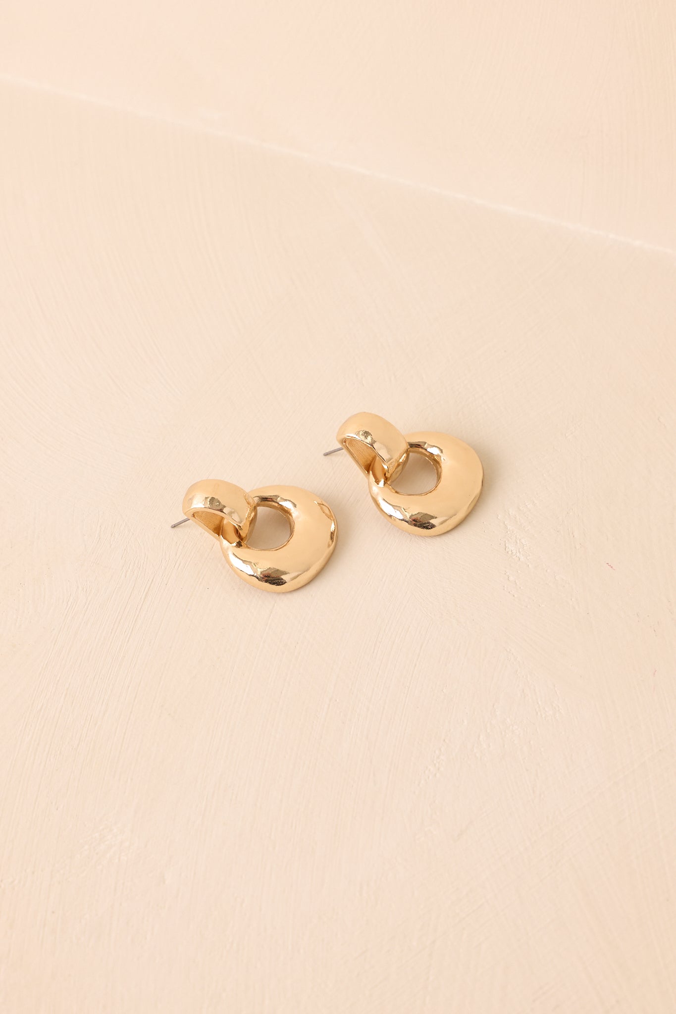 An angled view of the gold earrings highlighting the polished studs and circular drop link connection.