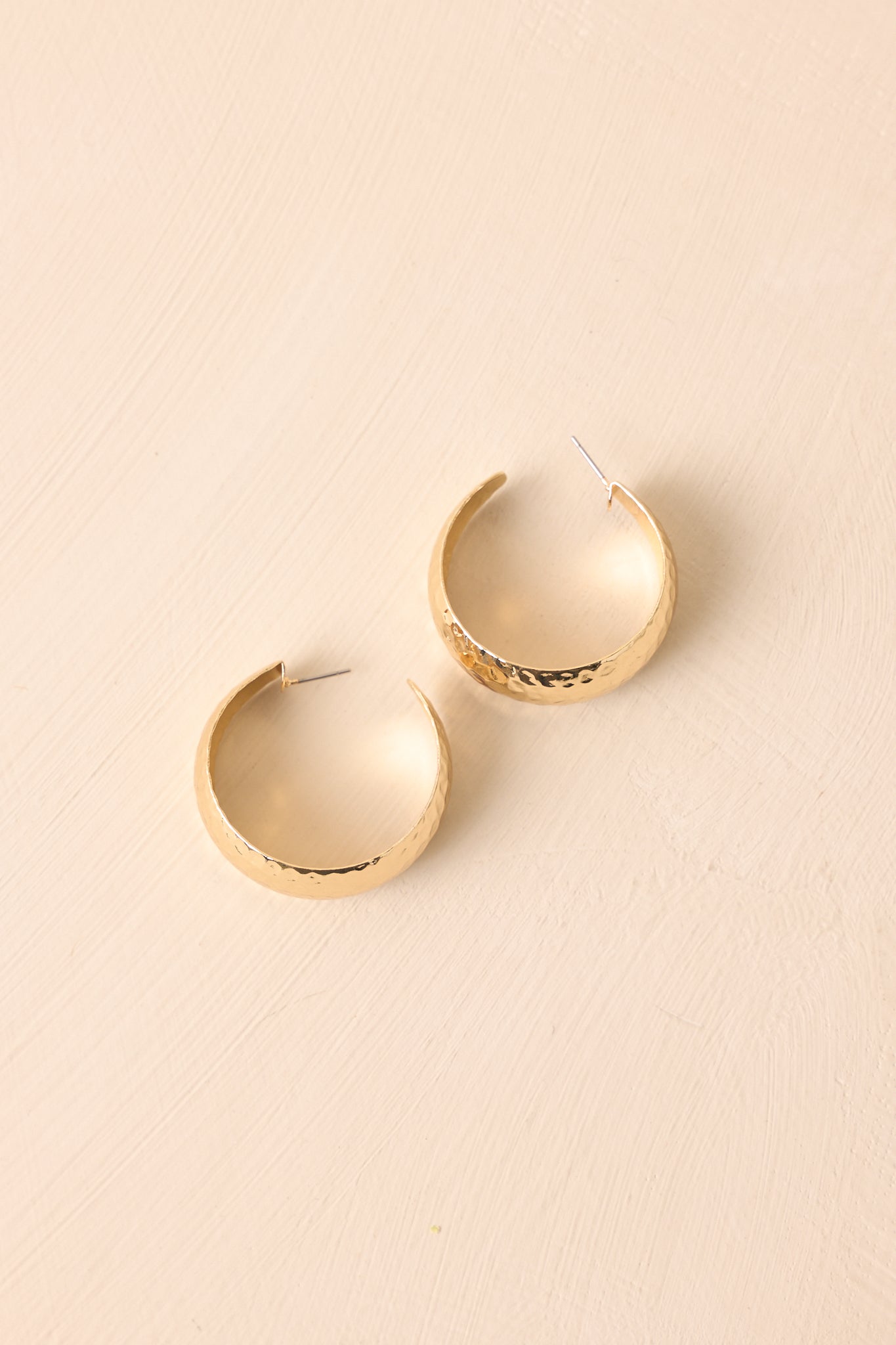 A cropped view of the gold earrings with a hammered texture and slightly tapered open hoop design.