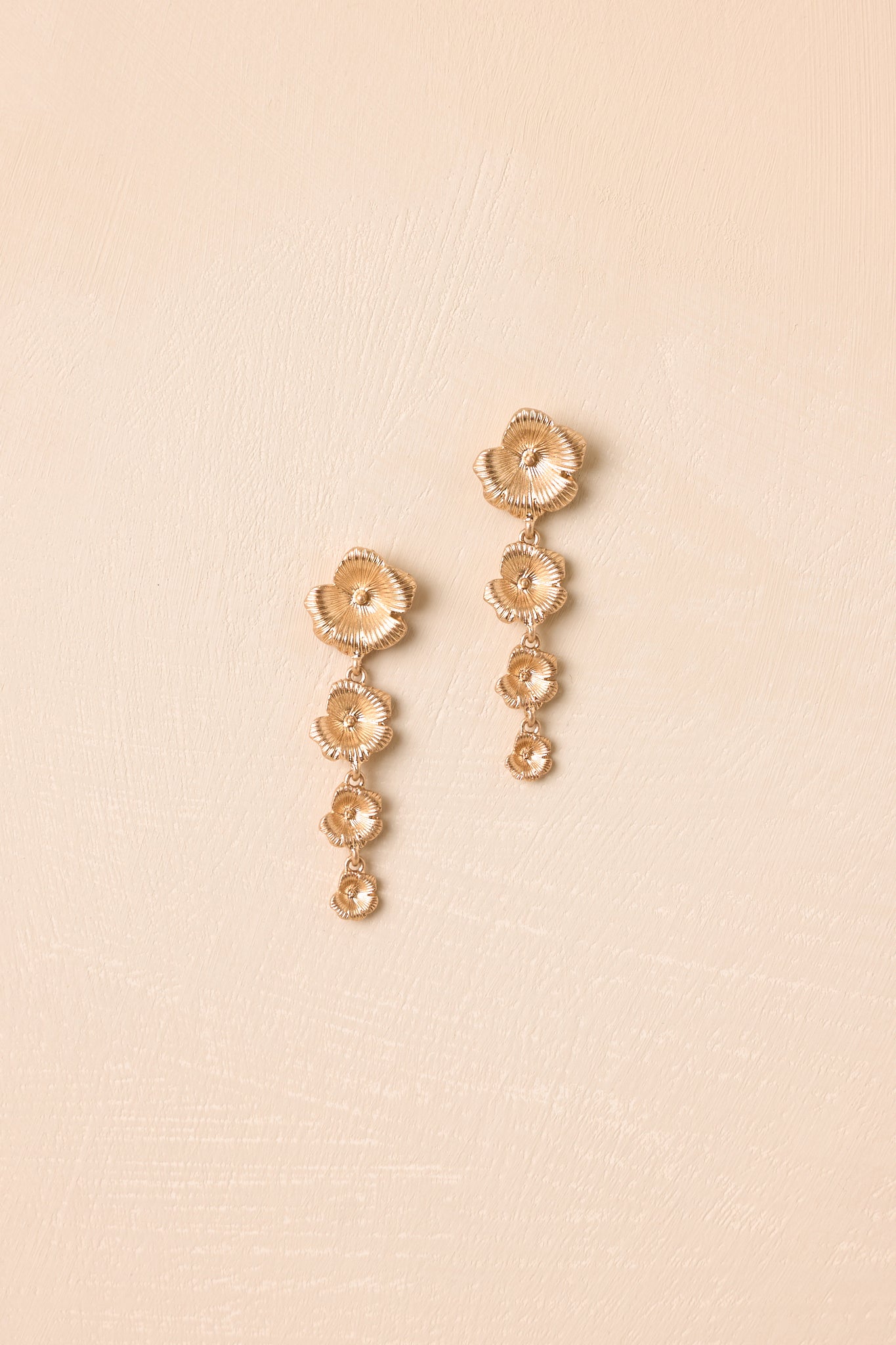 Front view of gold floral earrings displayed on beige background emphasizing layered bloom design.