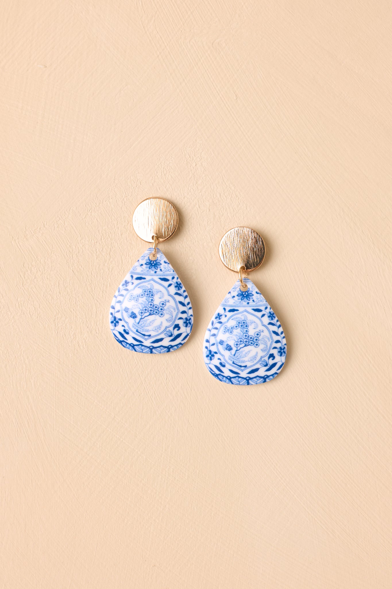 Gold-tone floral teardrop earrings displayed against a beige background with textured details and elegant styling.