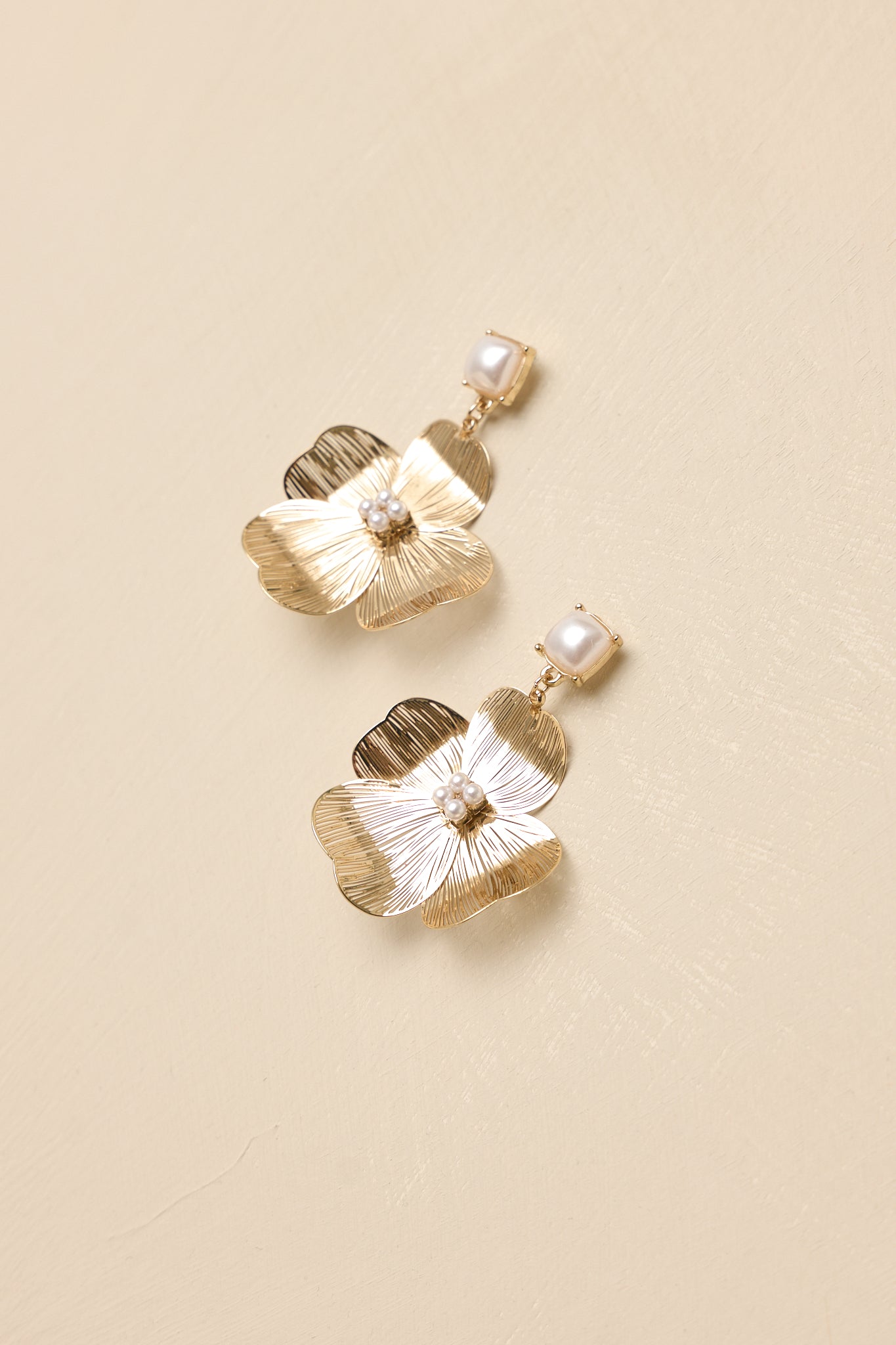 Close-up of gold flower earrings showing delicate textured petals and small pearl clusters for a refined floral design.