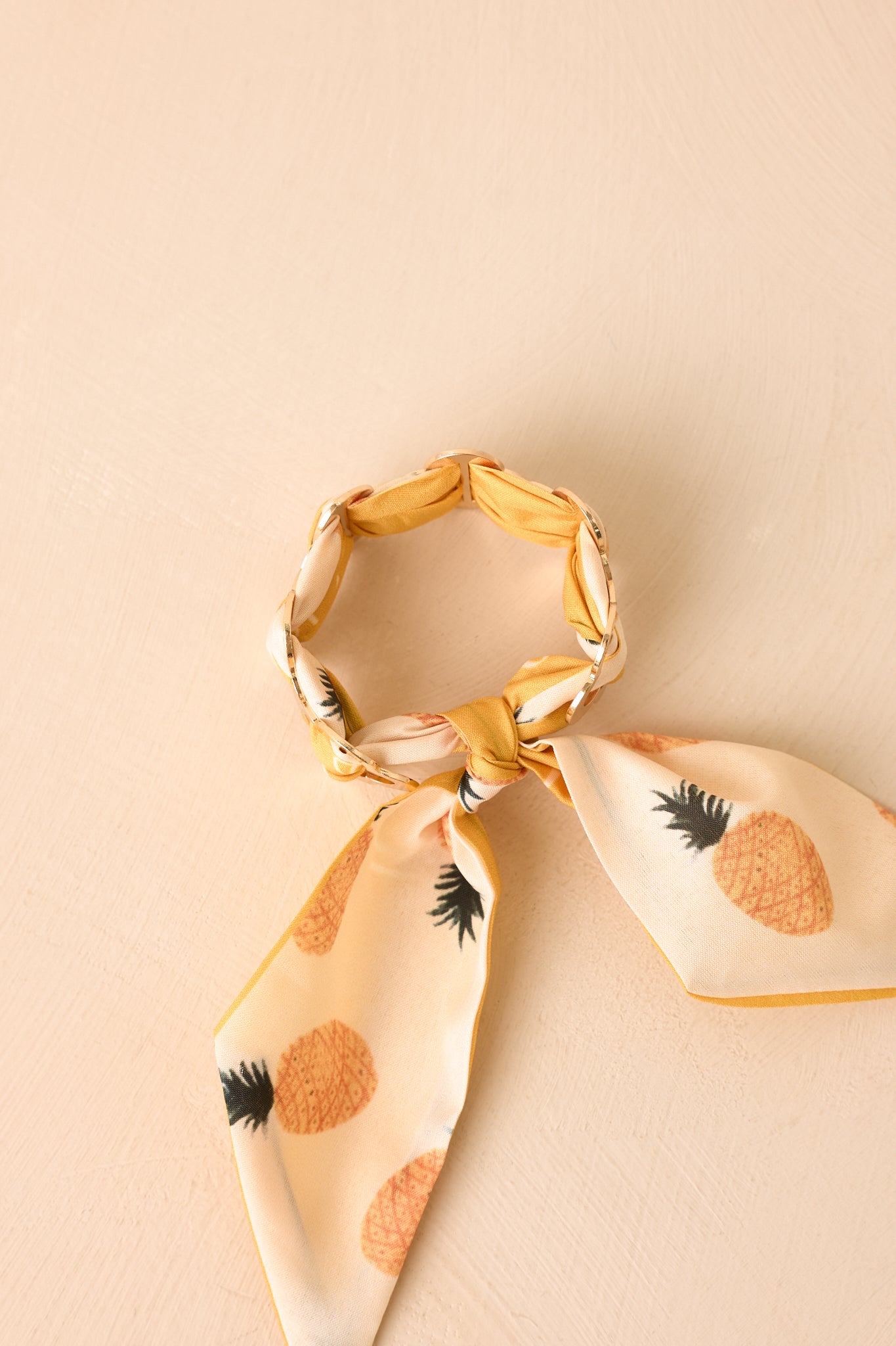 Gold geometric cuff bracelet displayed against a beige background with a vibrant yellow and ivory scarf accent.