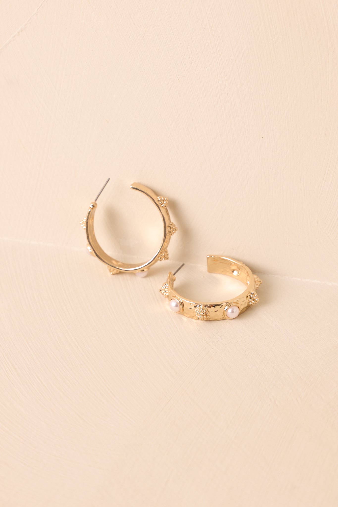A shot of the gold hoop earrings shown against a beige backdrop featuring evenly spaced pearls and half-sphere details.