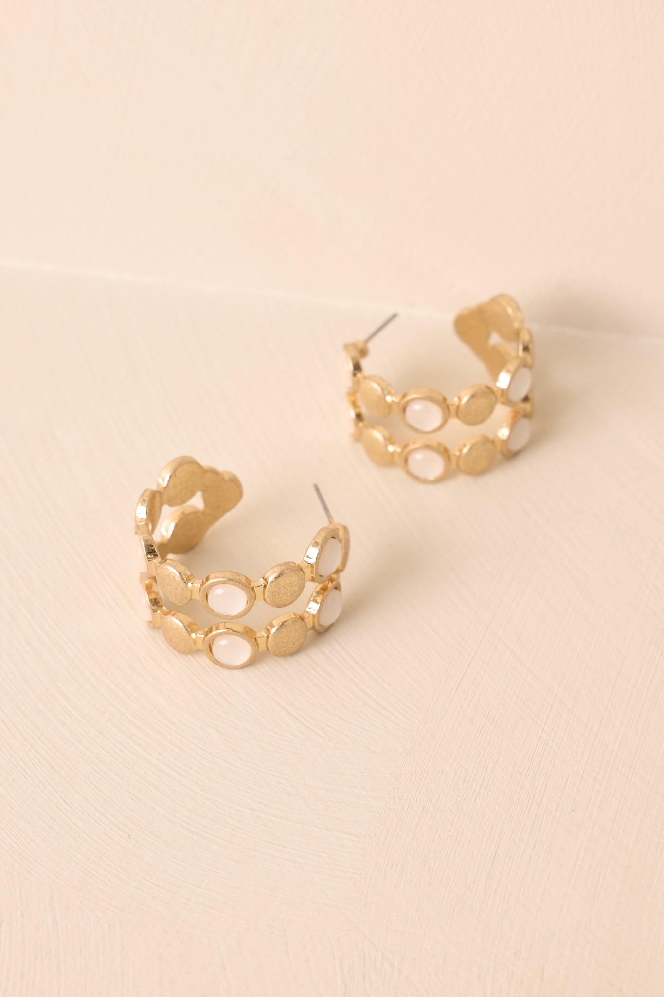 A detailed shot of the gold hoop earrings highlighting the textured discs and alternating iridescent stones.