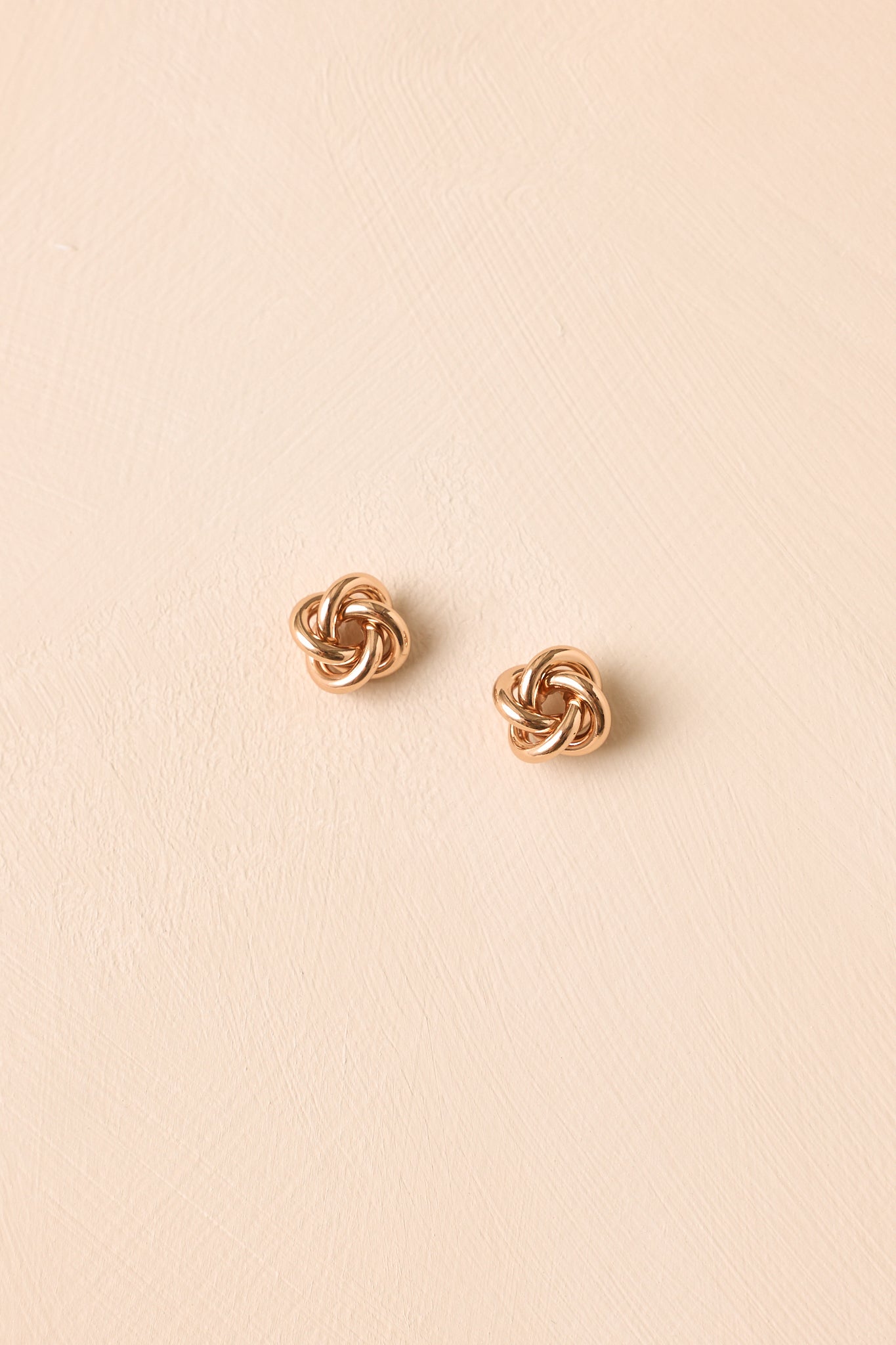 Gold knot stud earrings displayed against a neutral background, featuring a classic rounded shape and reflective polished finish.